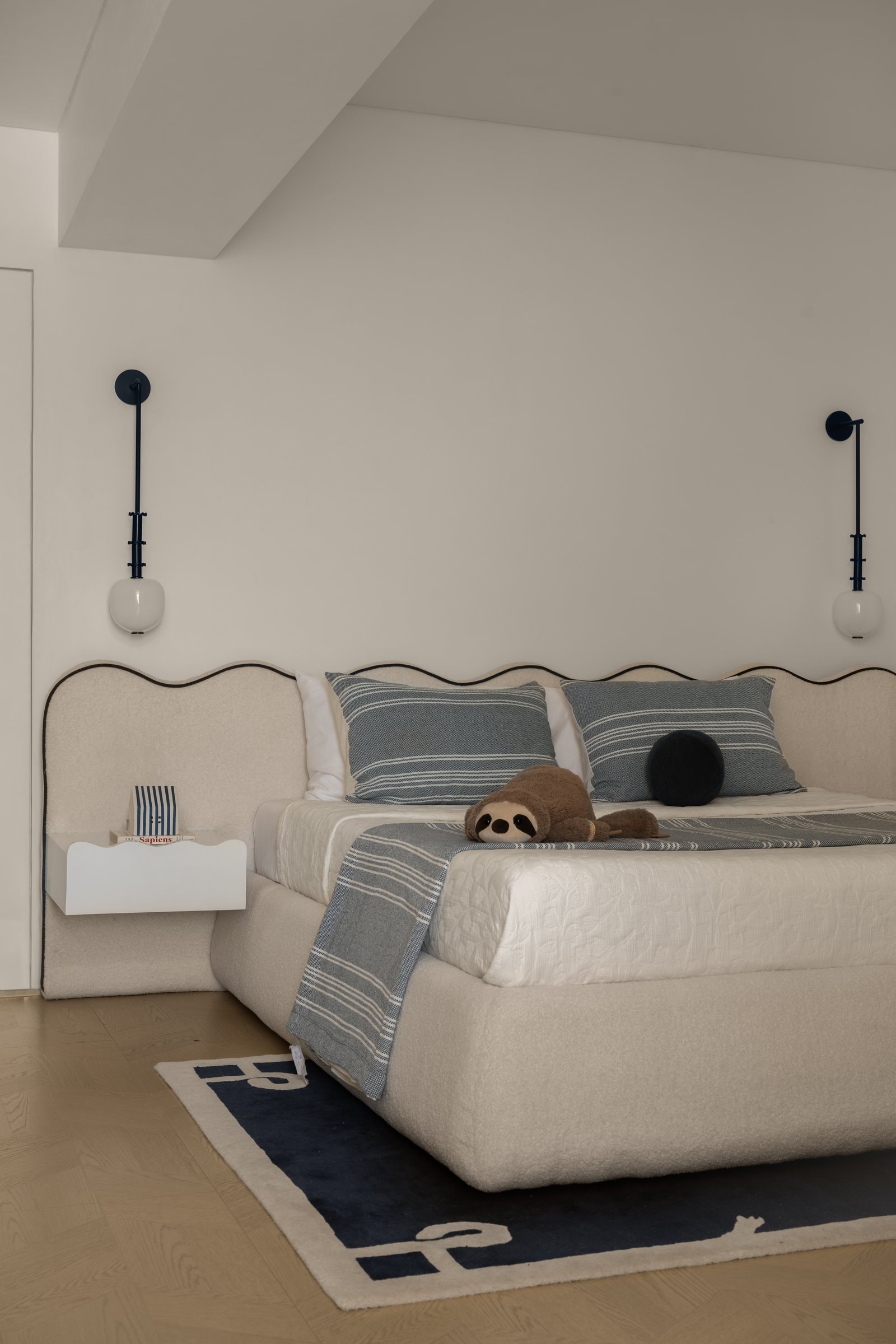 A wider view of the bed, where paired wall sconces and a striped textile palette give the room its coastal calm