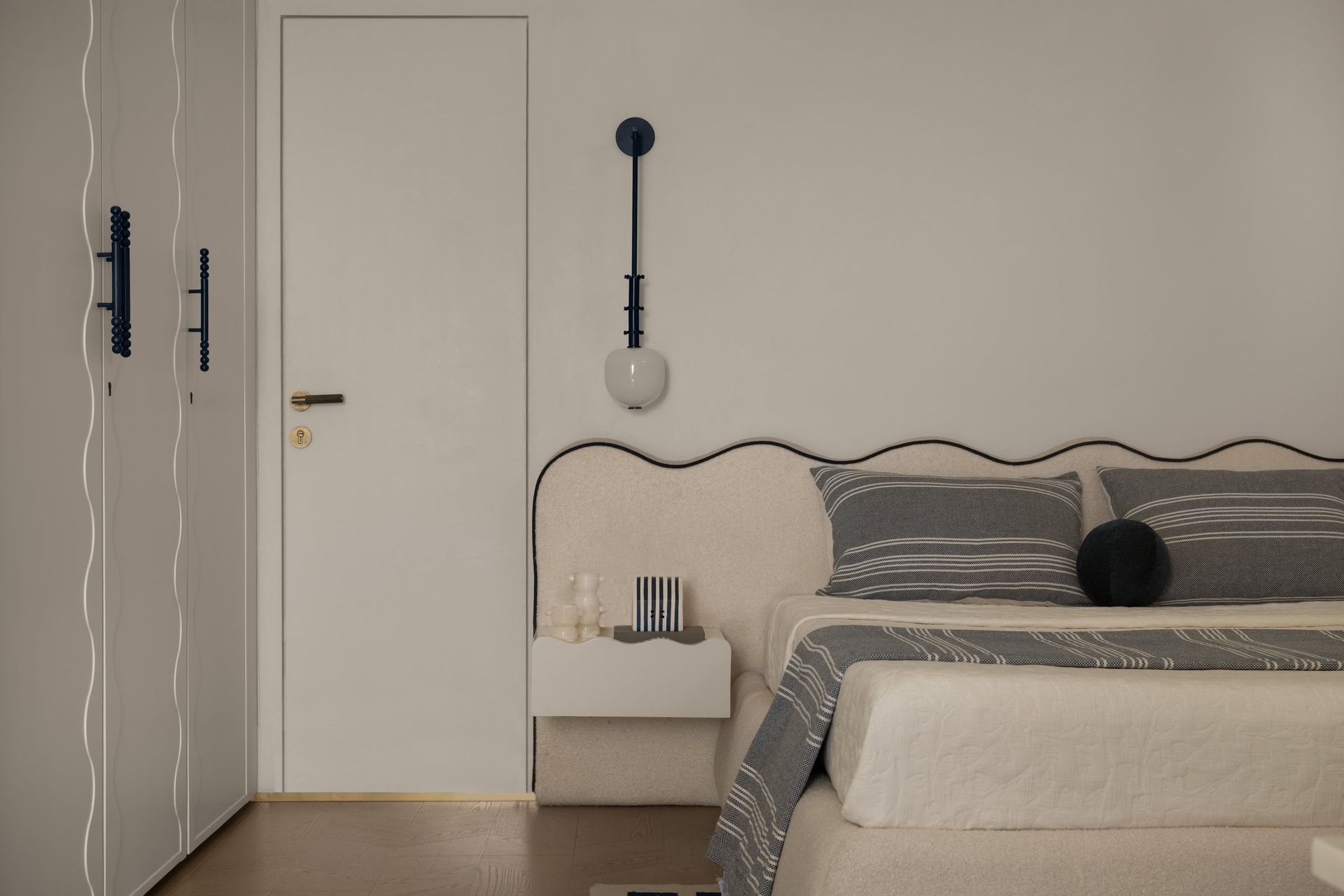 The master bedroom, where a scalloped upholstered headboard and a sculptural wall sconce establish the room's gentle geometry