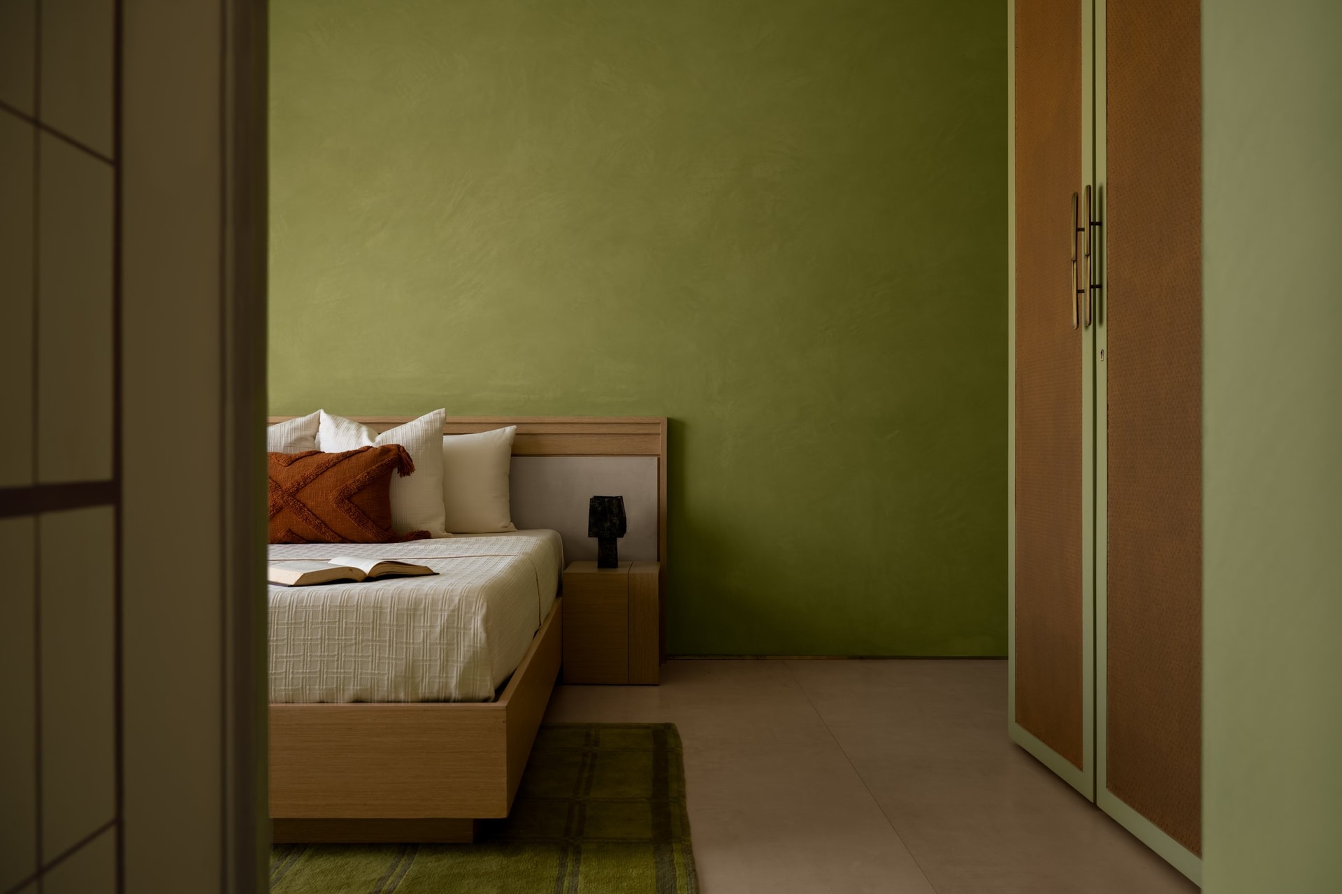 The green bedroom, where an olive-toned lime wash envelops the room and a cane-fronted wardrobe softens the palette