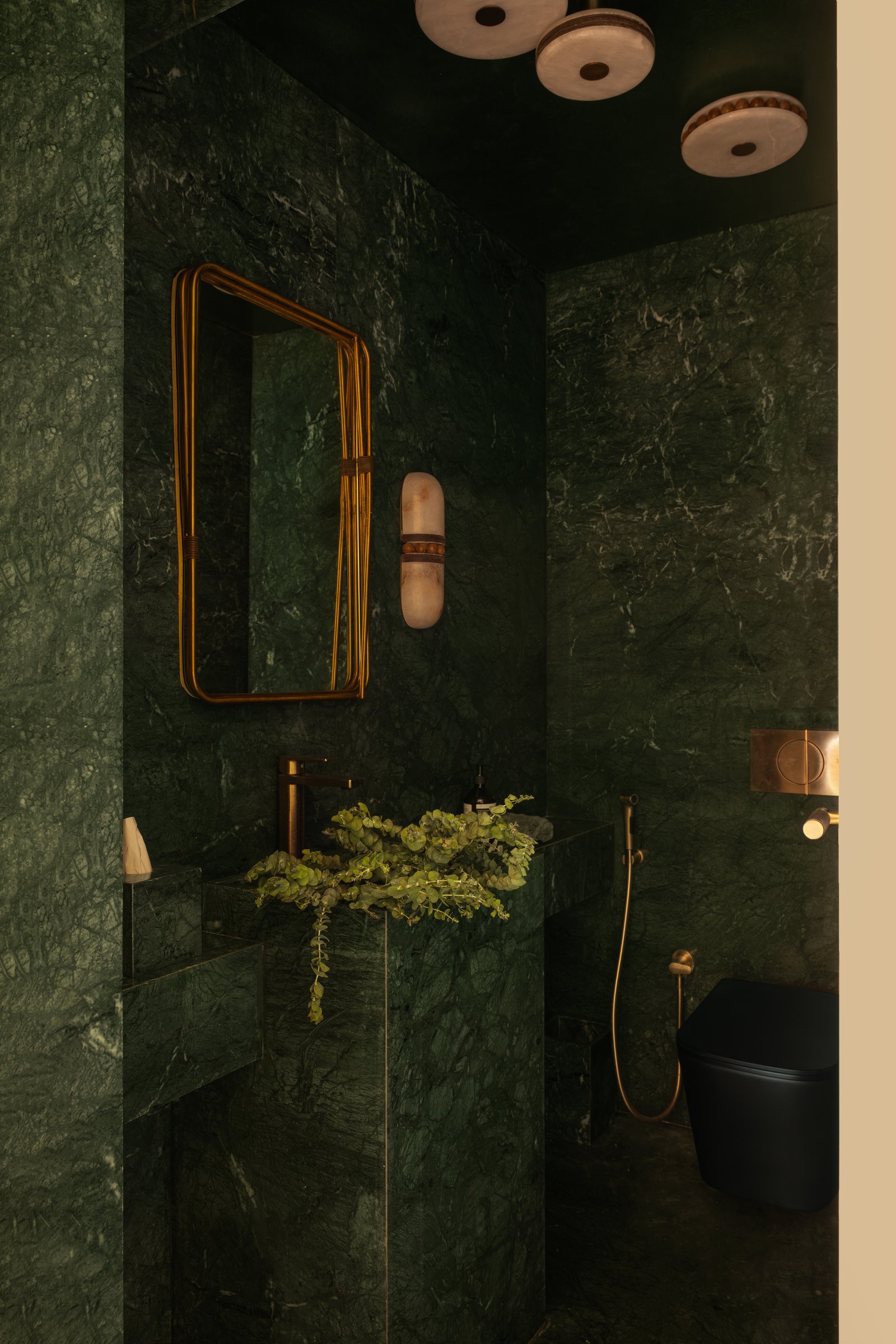 The powder bathroom, where dark green stone envelopes the volume and alabaster fixtures introduce a luminous counterpoint