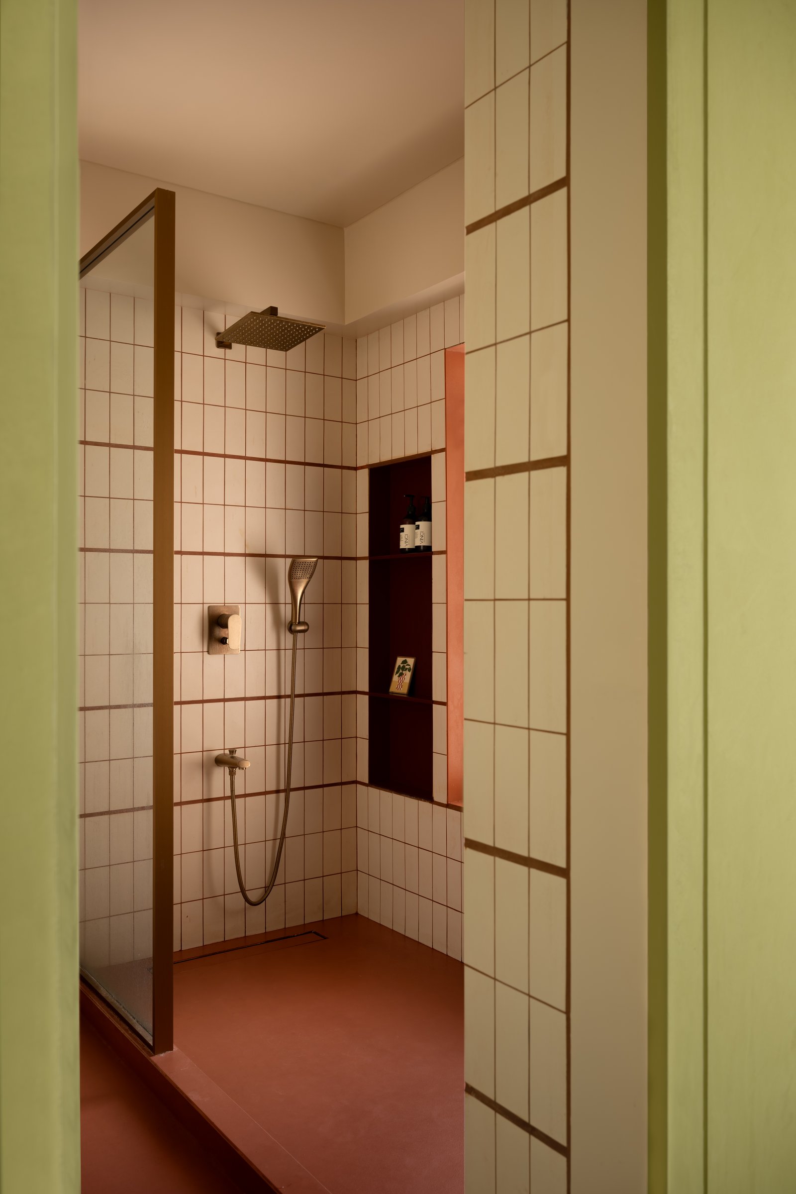 The green tiled shower, where slim ceramic tiles and a burgundy niche introduce a rhythmic geometry