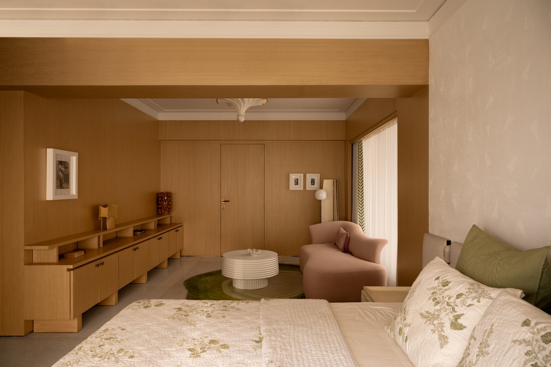 The parents' bedroom, where a warm wood console and a rounded blush armchair introduce a softer, more layered domesticity