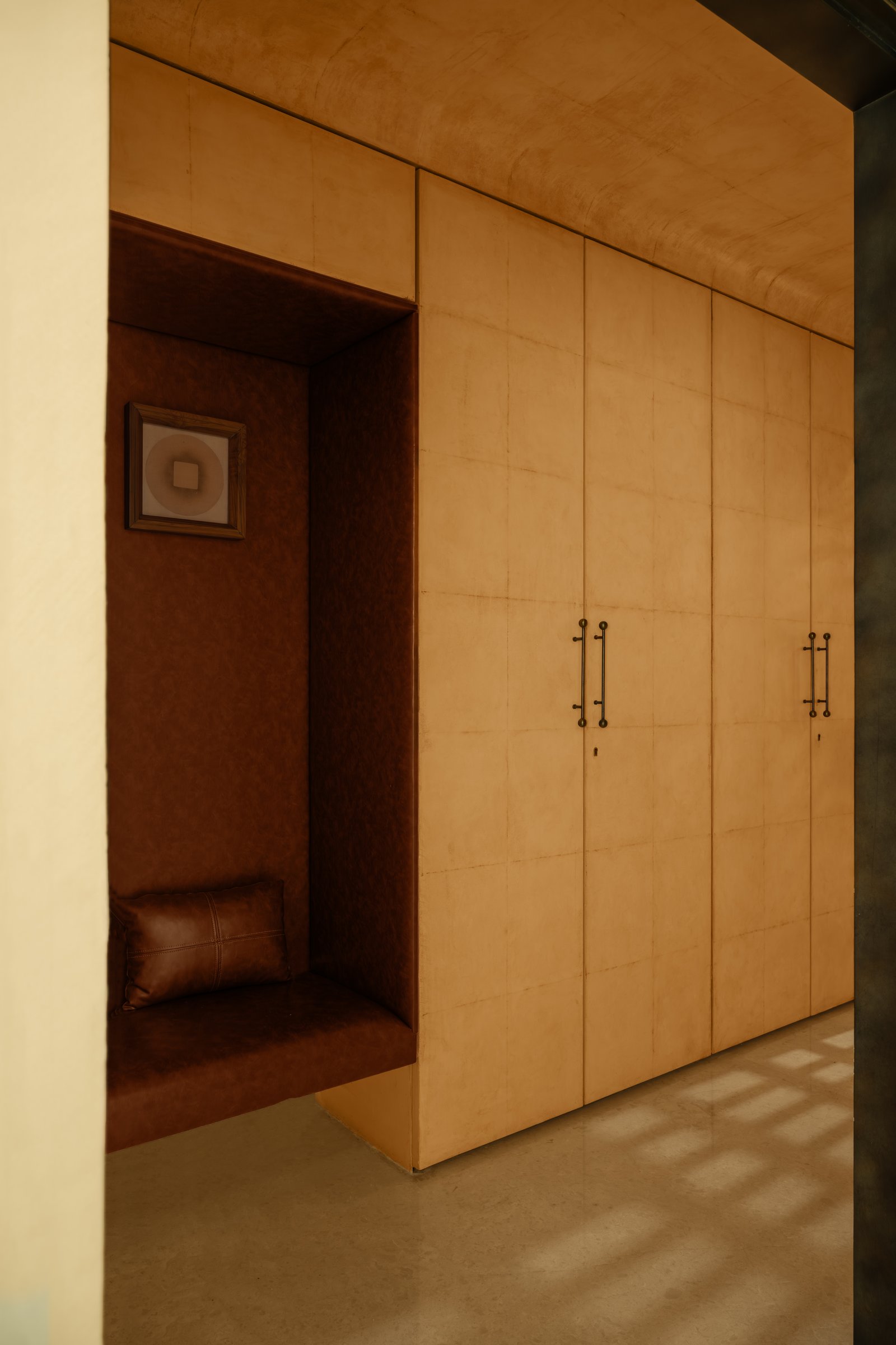The foyer, where a leather-upholstered niche is set into a wall of concealed storage, transforming utility into a quiet architectural moment