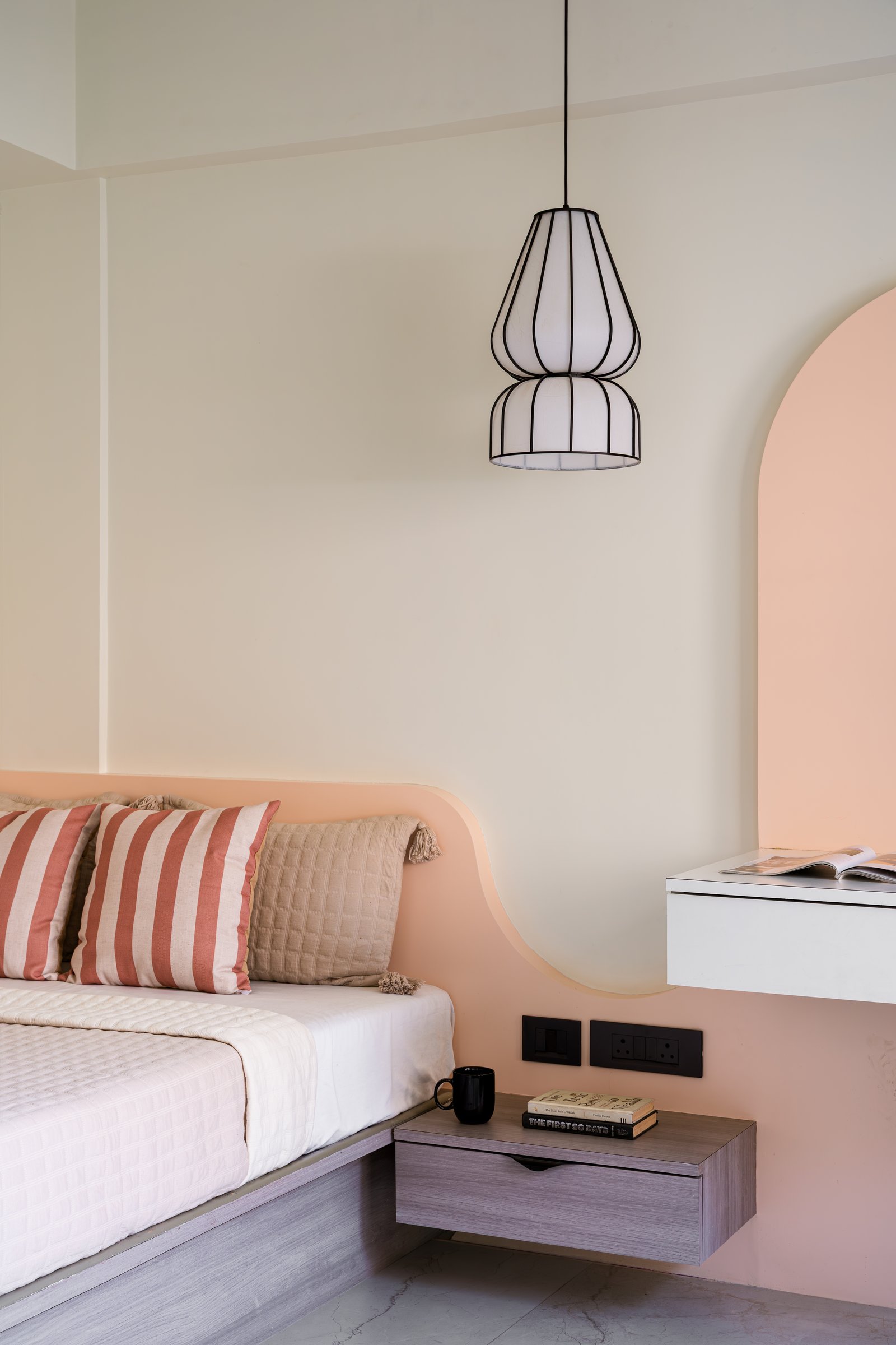 The daughter's bedroom, where the curved headboard band, cage pendant, and arched niche form a single gentle composition