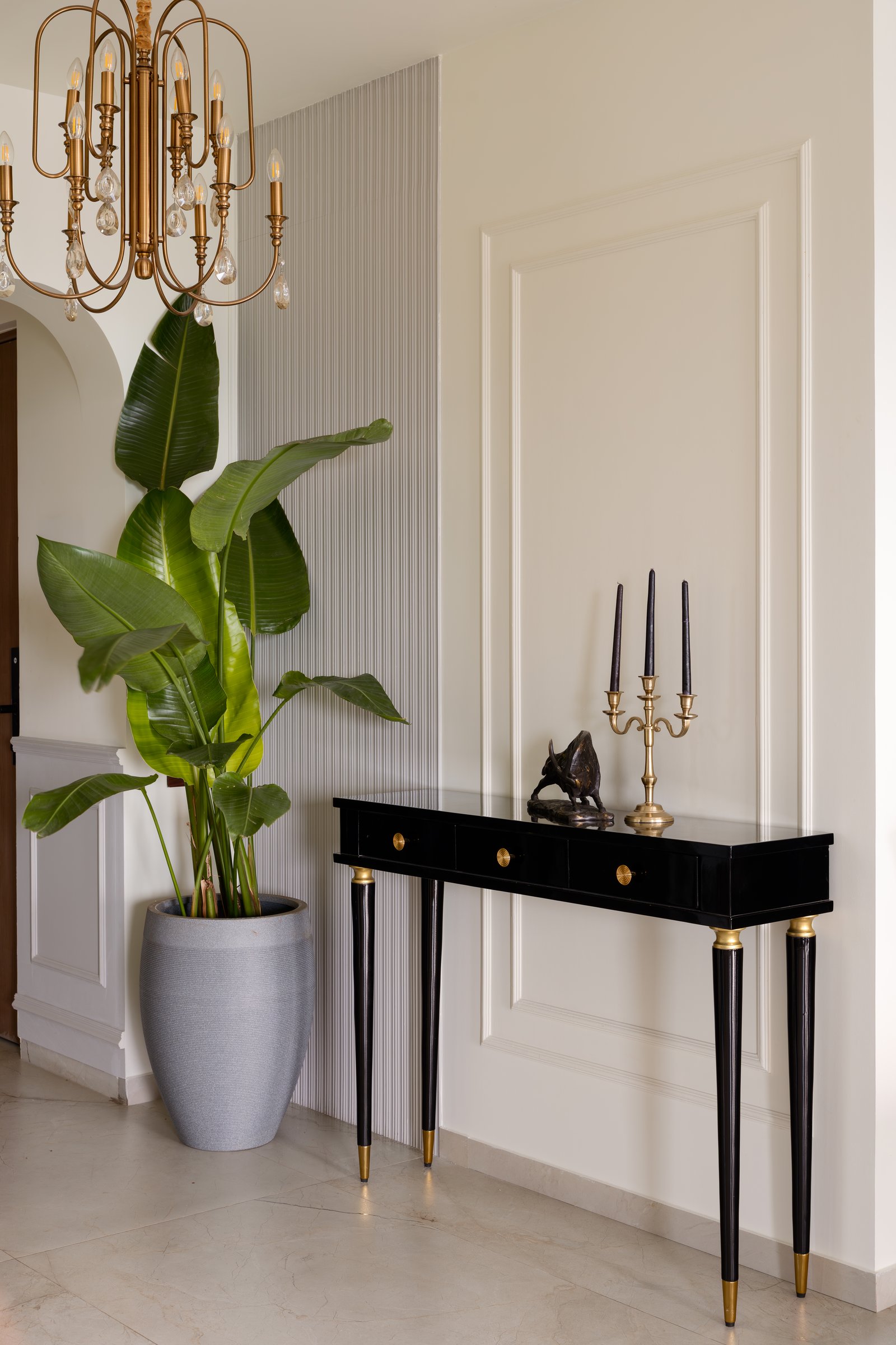 The foyer, where a fluted panel and a lacquered black console with brass-tipped legs establish the home's material language