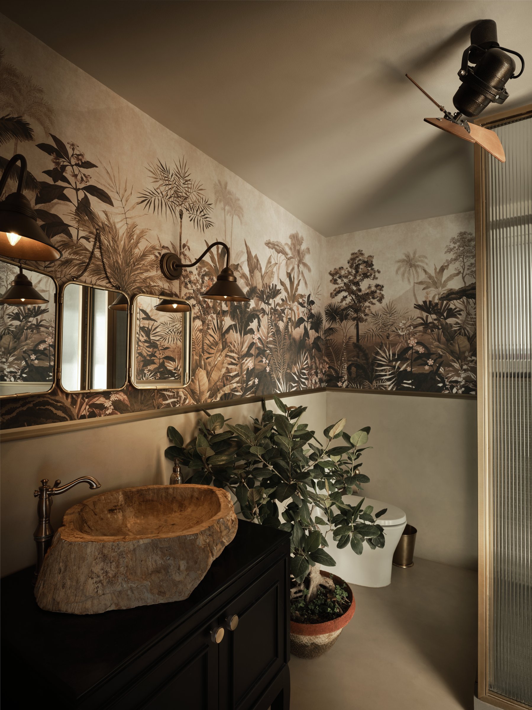 The powder room, where a sepia jungle mural meets brass-framed mirrors above a hewn wooden basin