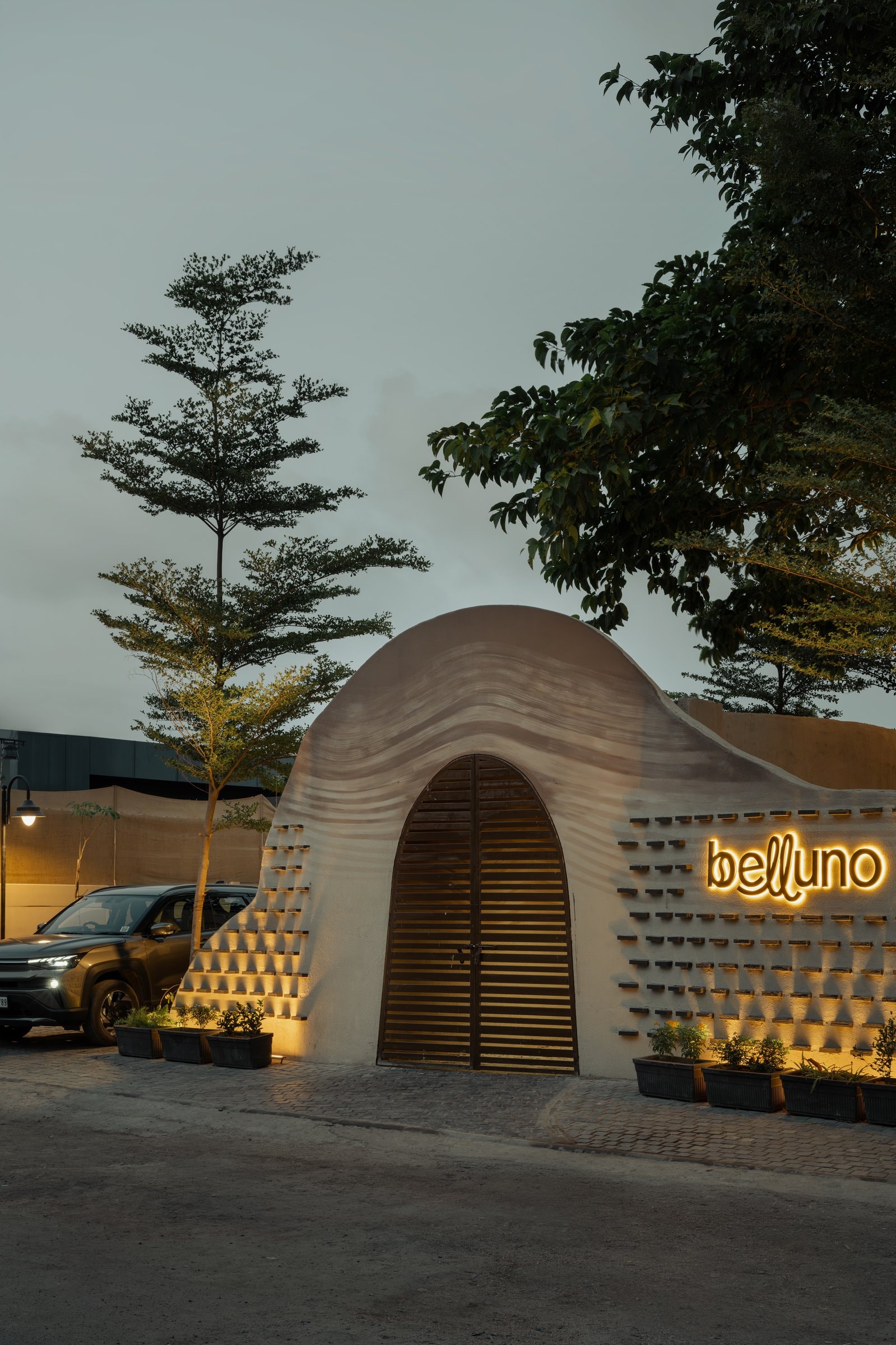 The dune-like plaster façade rising from the street, its ribbed surface and backlit signage giving the frontage a soft, sculpted silhouette