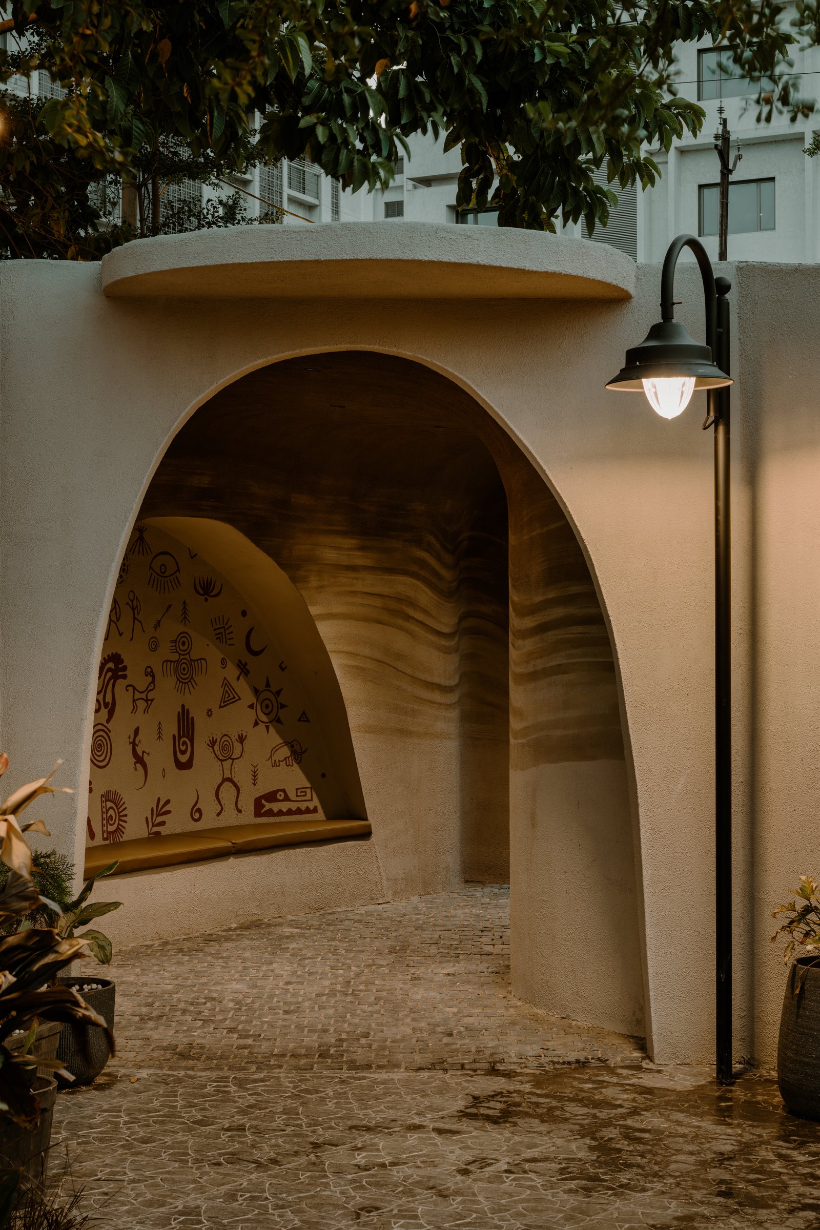 The curved plaster threshold at Belluno's outer boundary, its pictographic mural setting the café's earth-toned register before arrival