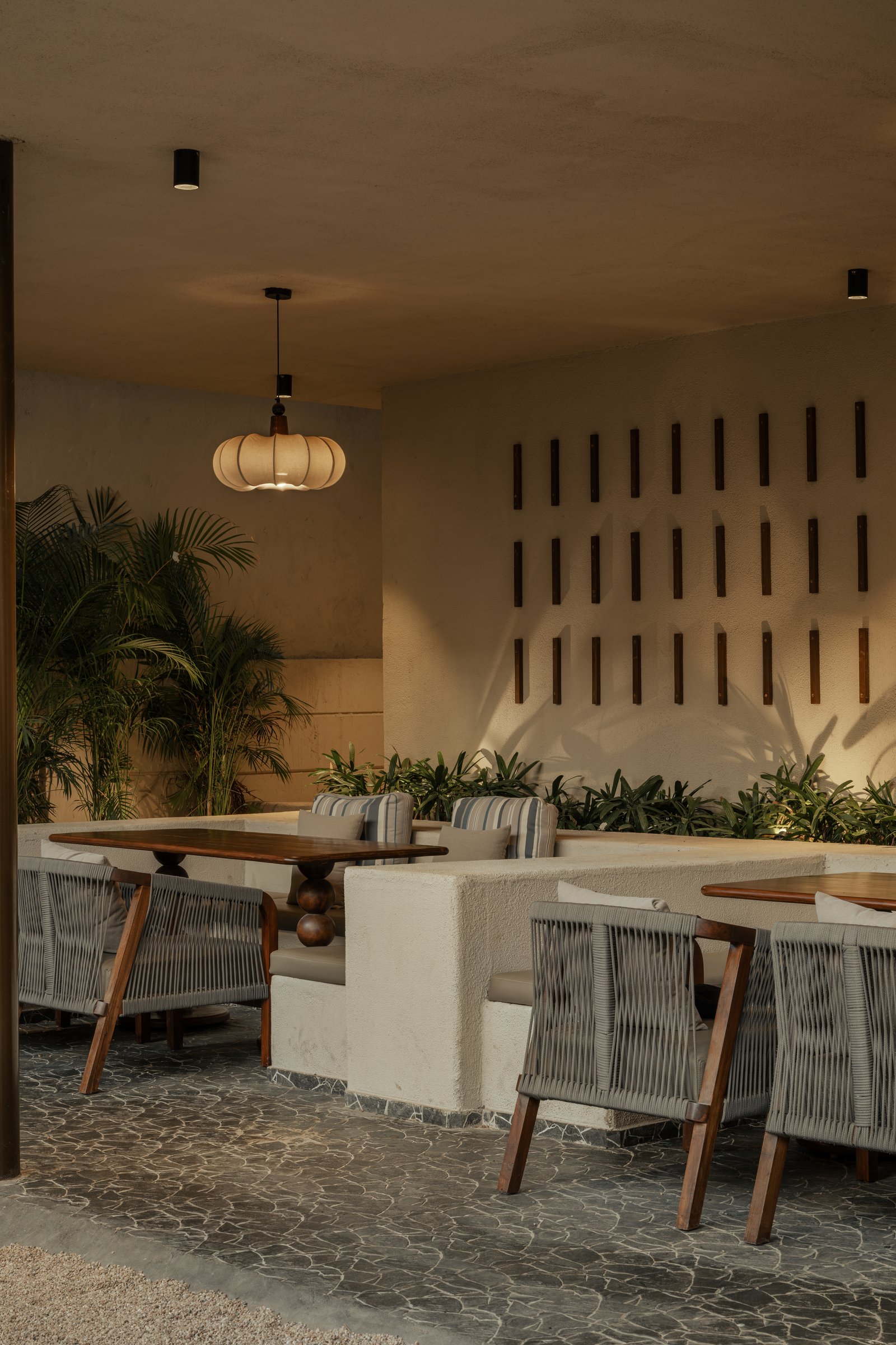A covered dining pocket where a raised plaster banquette and rope-backed chairs sit beneath a scalloped fabric pendant