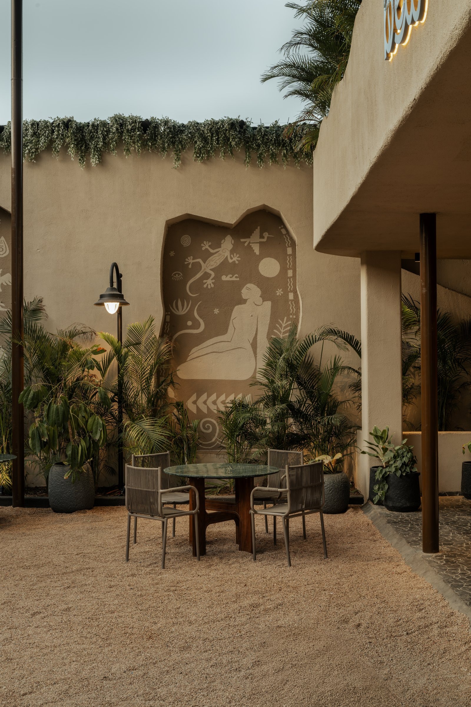 A gravel-set seating pocket anchored by a folk-inspired mural that threads pictographic sensibility through the outdoor rooms