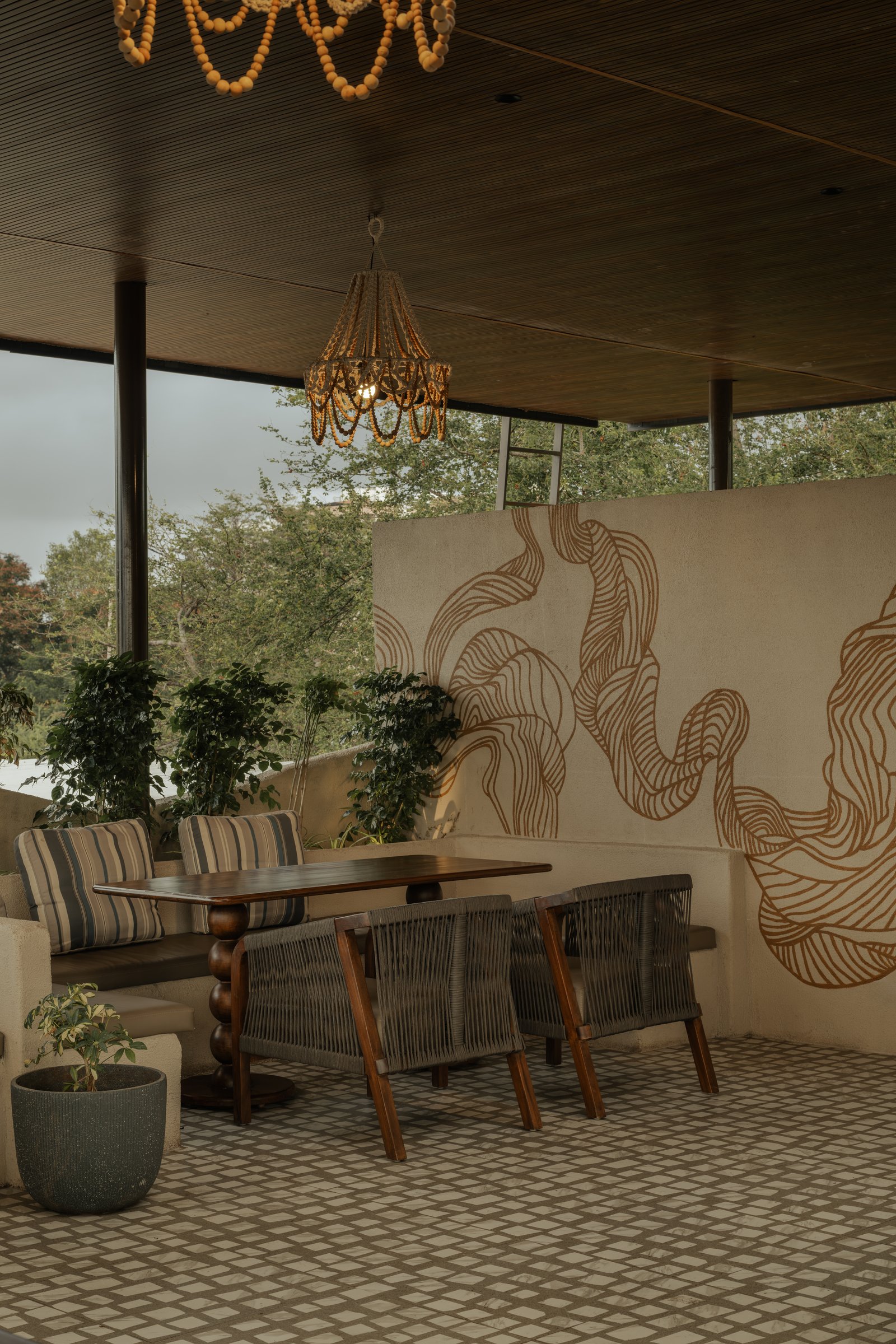 A linear banquette on the covered deck, set against a terracotta-line mural whose curves echo the café's overall geometry