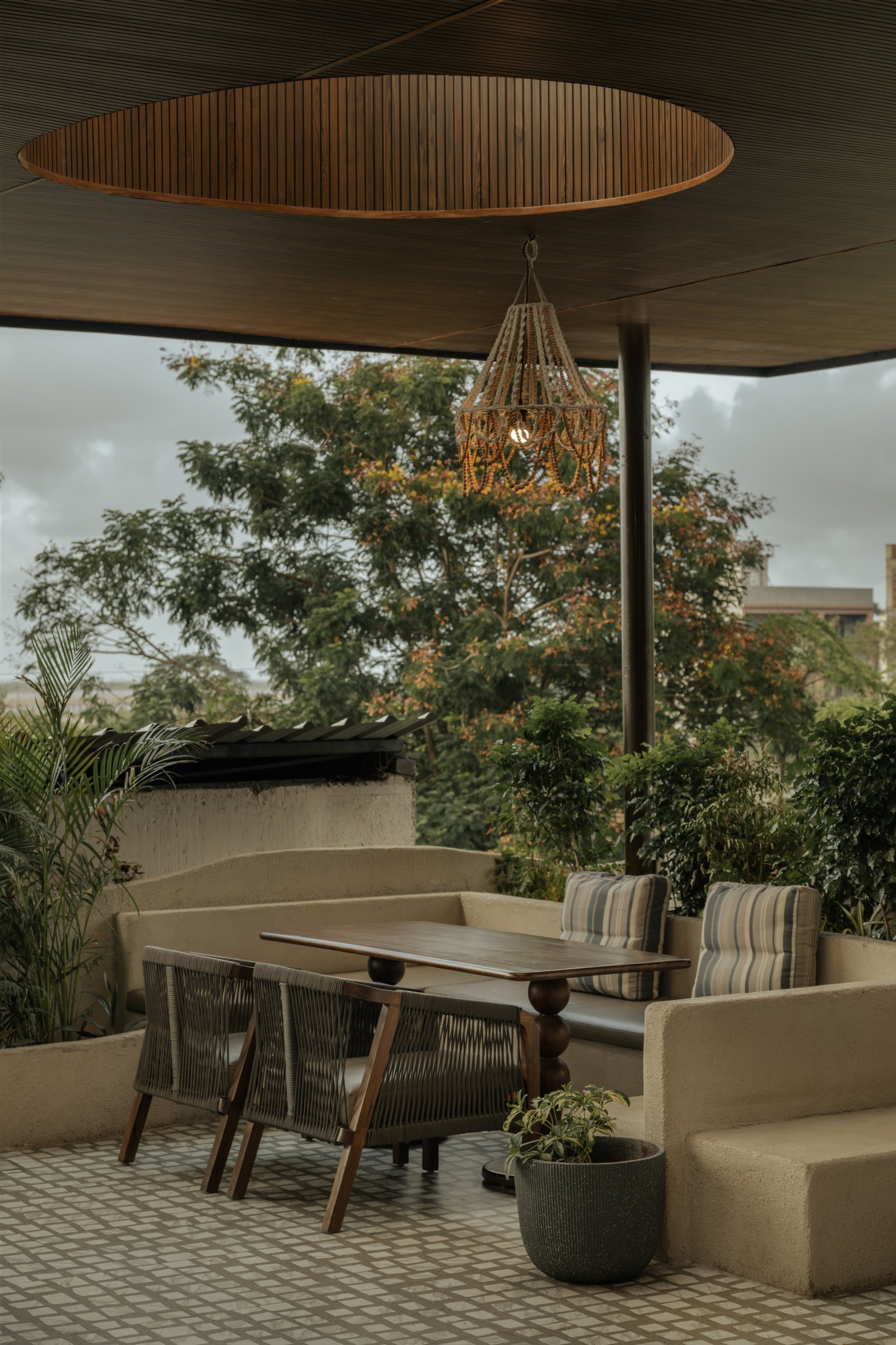 The circular oculus above the deck's beaded chandelier draws sky and tree canopy directly into the seating composition