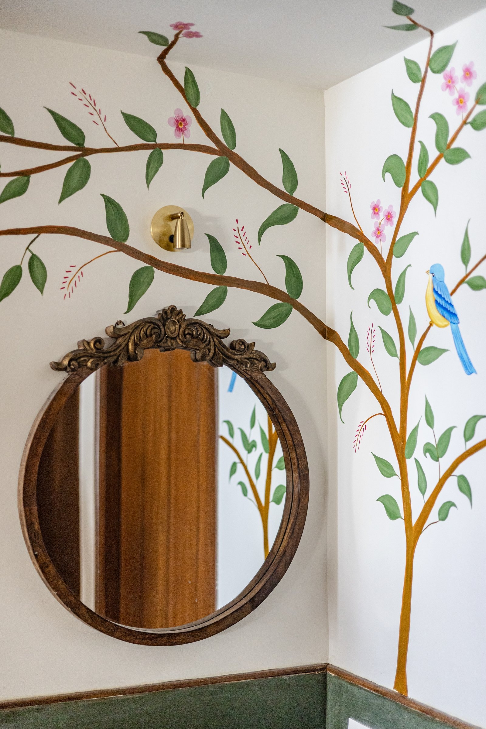 A hand-painted mural of a flowering tree meets a carved round mirror in a quiet corner