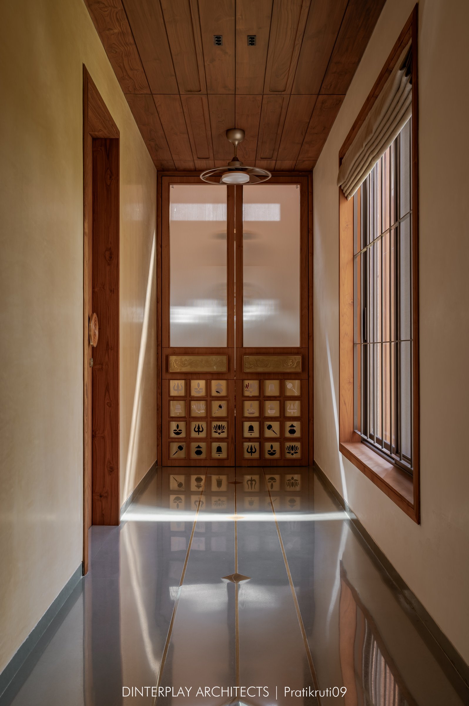 The mandir passage, where warm ochre walls and a brass-inlaid floor lead to reeded-glass devotional doors