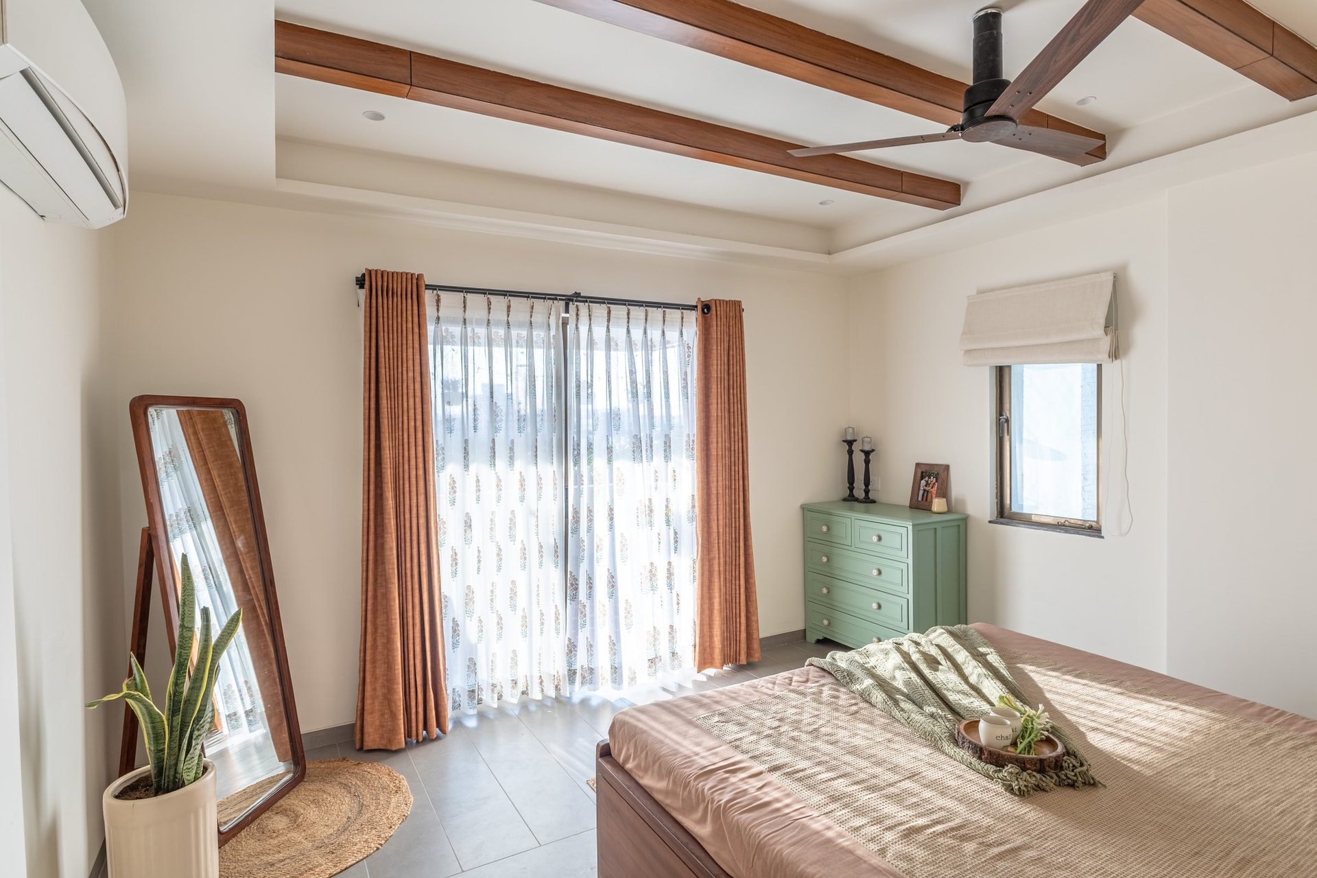 The primary bedroom, where a coffered beam ceiling and rust-toned block-printed sheers set the register