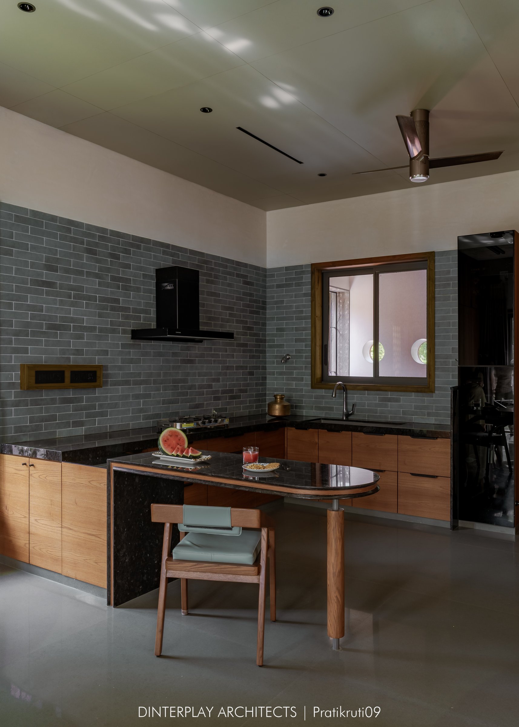 The kitchen, with grey brick-format tile, warm timber fronts and a small oval breakfast counter