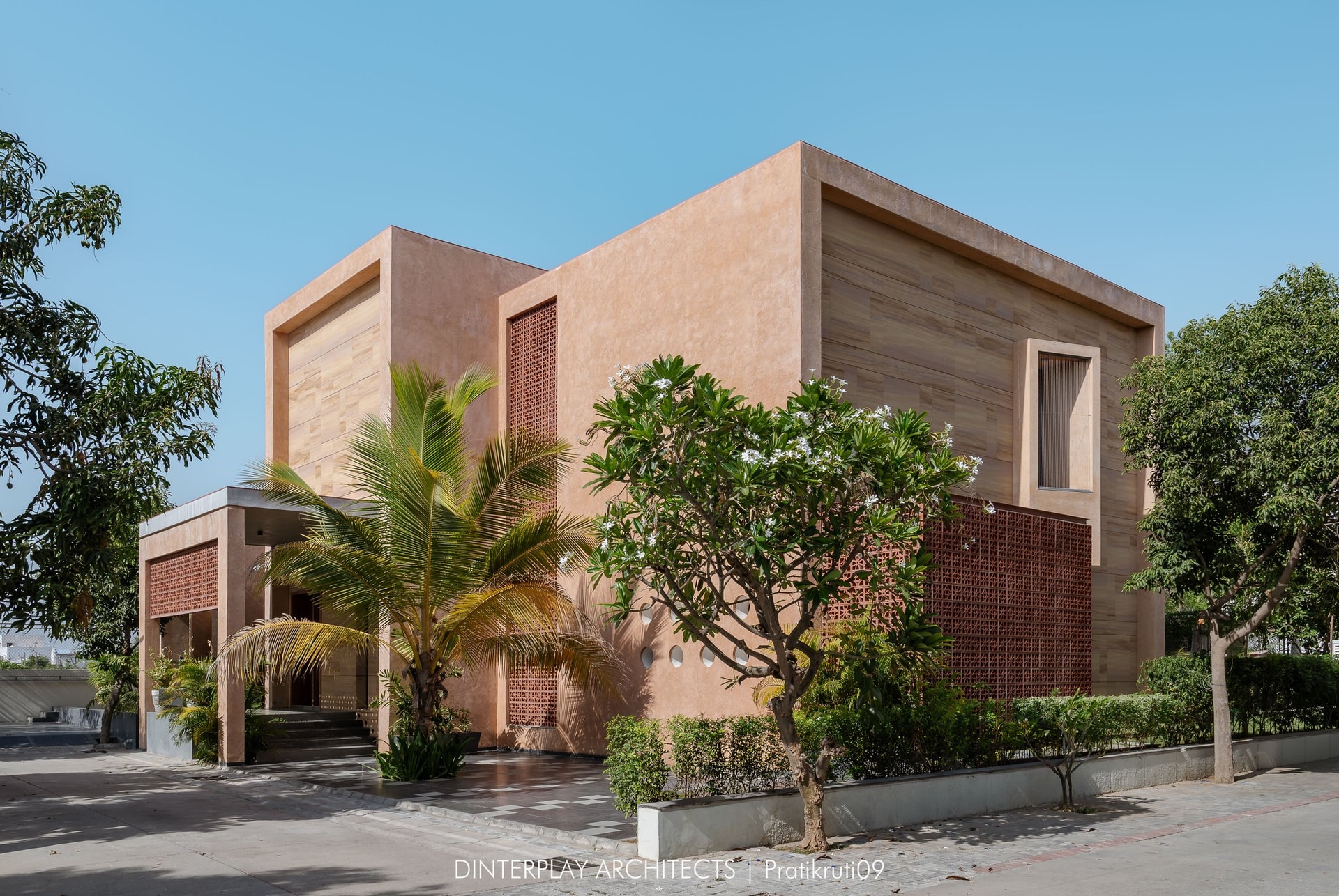 Seen from the street corner, the residence reads as a composition of plaster-clad volumes softened by mature planting