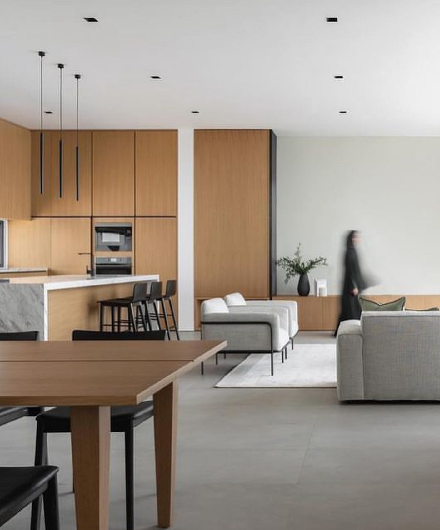 The kitchen opens into the living and dining volume, unified by warm cabinetry and a pale concrete-look floor.