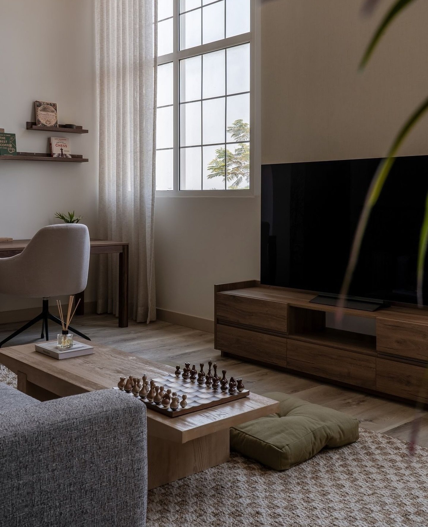 An arched sheer-dressed window casts diffuse light across wood floors and grey upholstery.