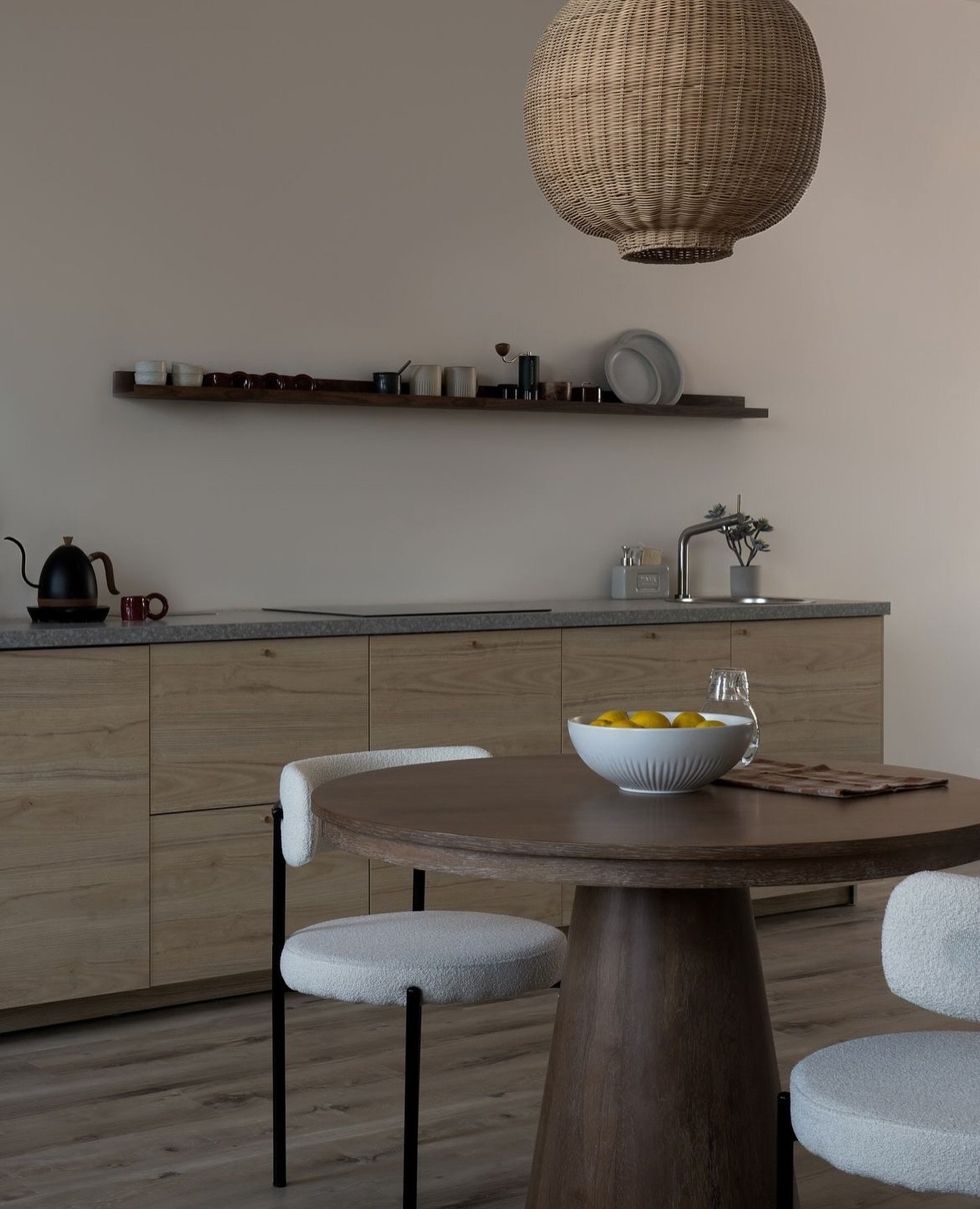 The pale wood kitchen run meets the dining table, softened by boucle chairs and honed stone.