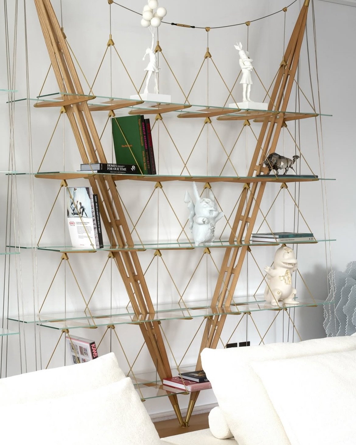 A bespoke shelving structure of wooden struts, brass tensioning cables, and floating glass shelves, the home's ethos in miniature.