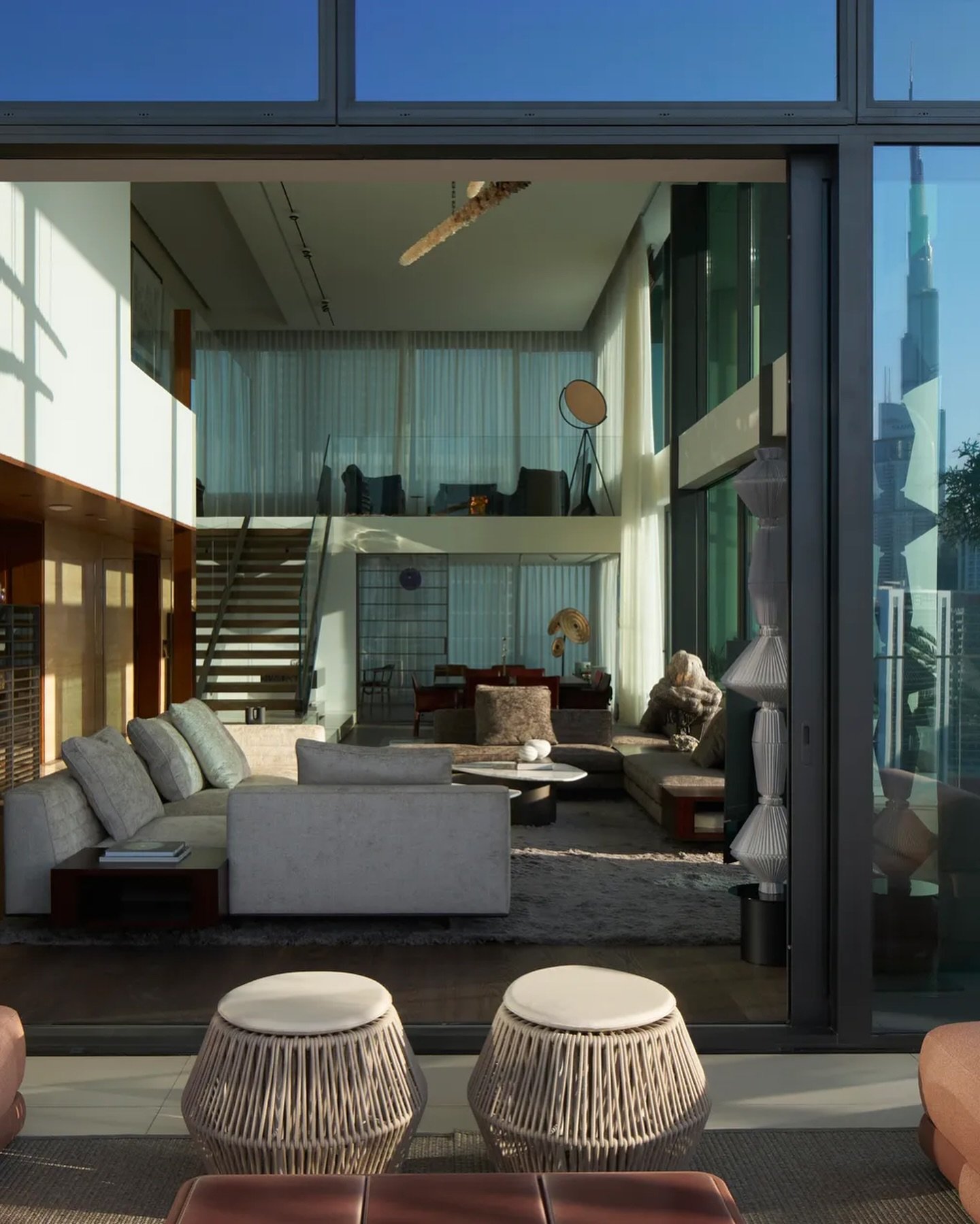 Seen from the terrace, the double-volume living room opens through full-height glass, with the Burj Khalifa faintly reflected.