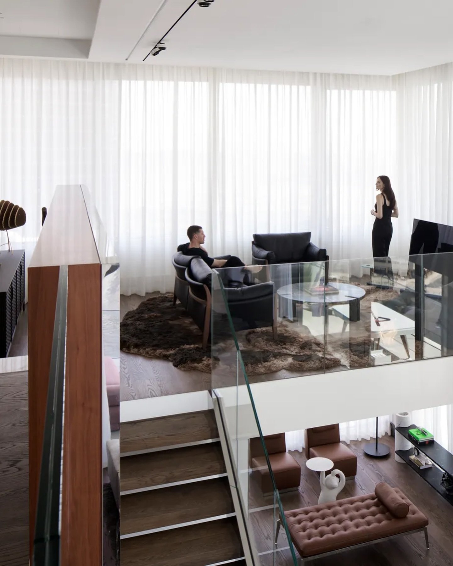 From the mezzanine, a glass-and-wood staircase ties the two levels together, resolving the home's spatial dialogue.