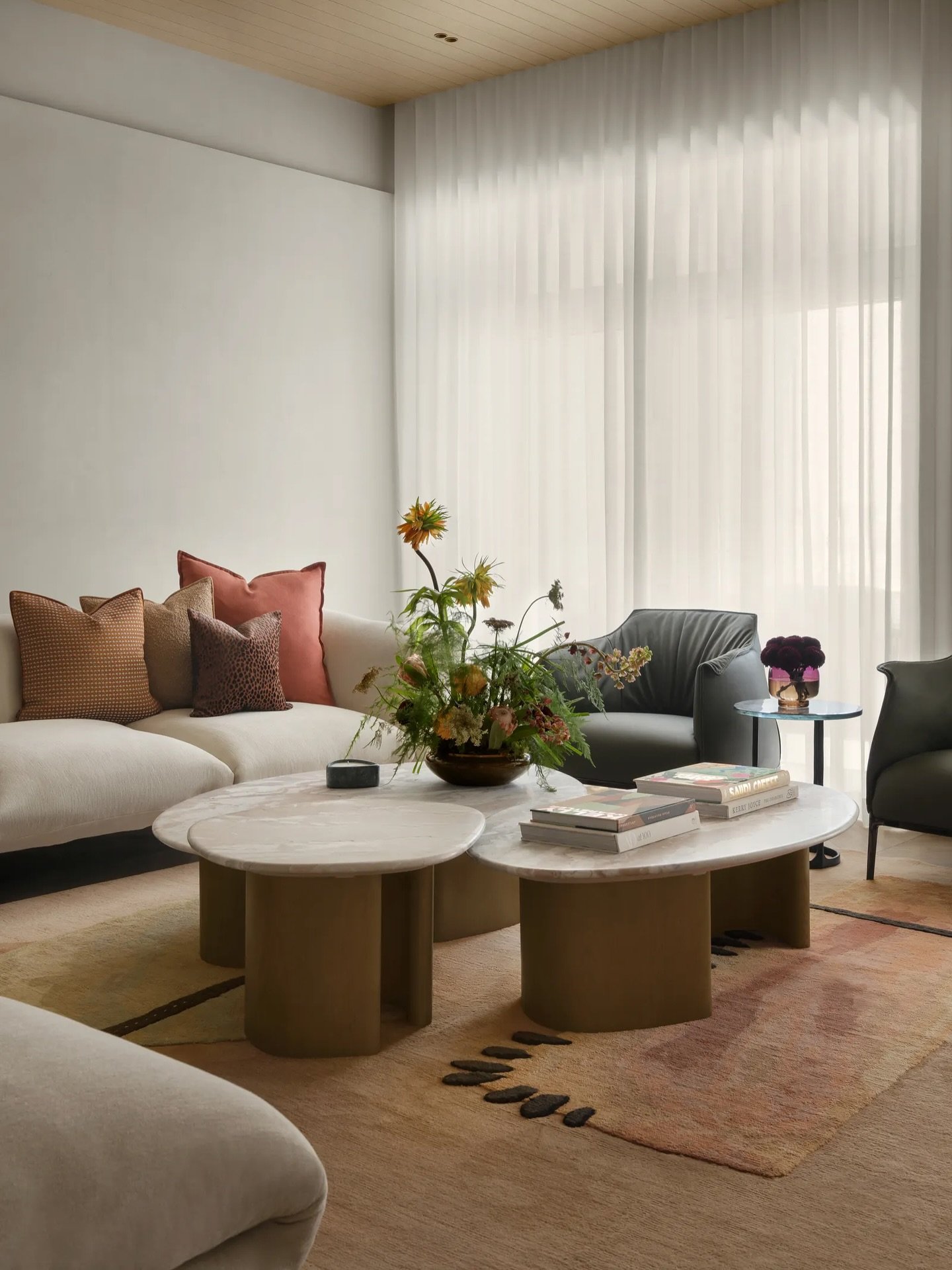 Fluted mustard-toned bases anchor marble-topped coffee tables before a deep cream sectional layered in rust and dusty pink.