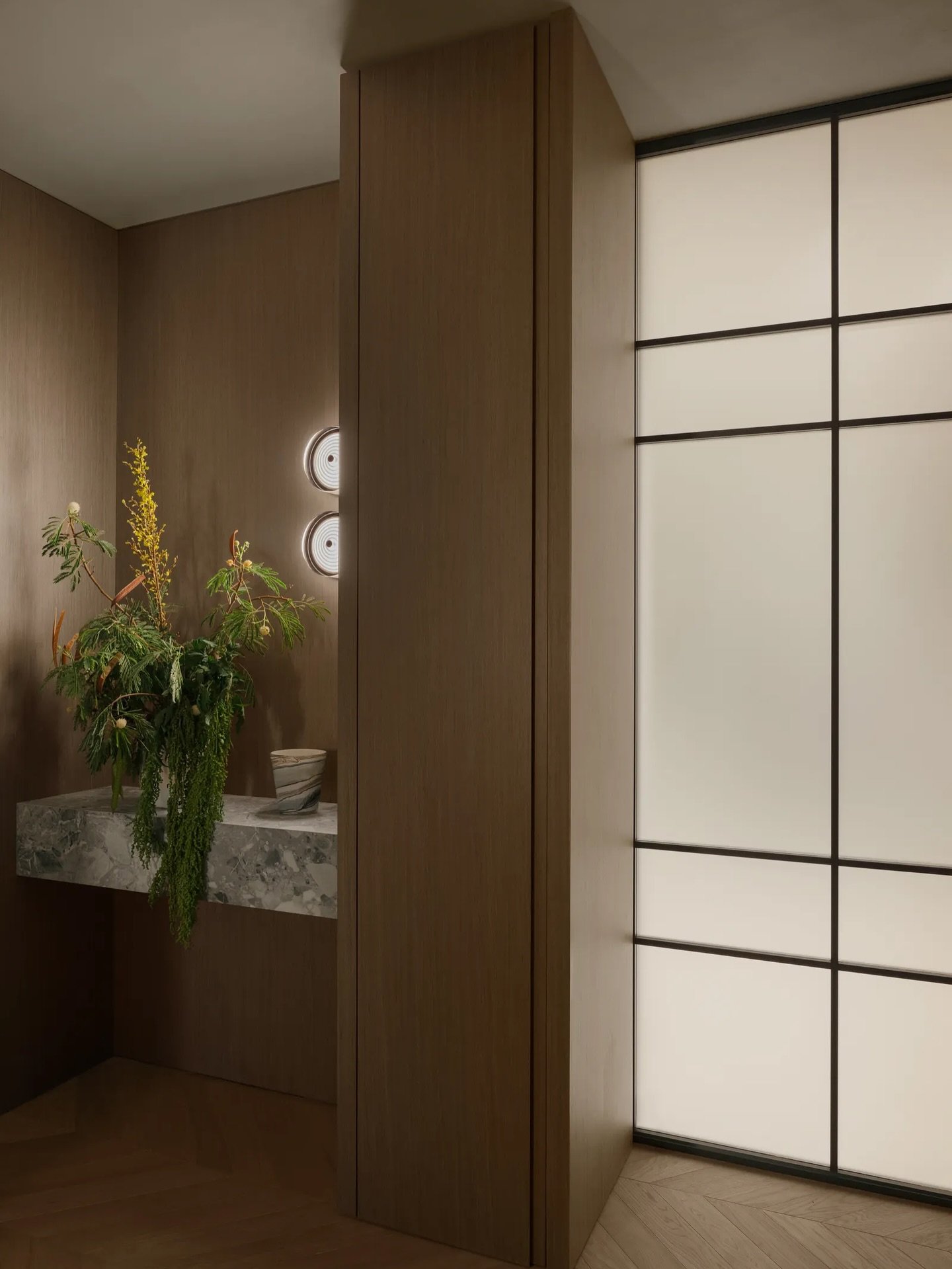A frosted Rimadesio pivot and backlit glass partition articulate the threshold between staff quarters and communal zones.