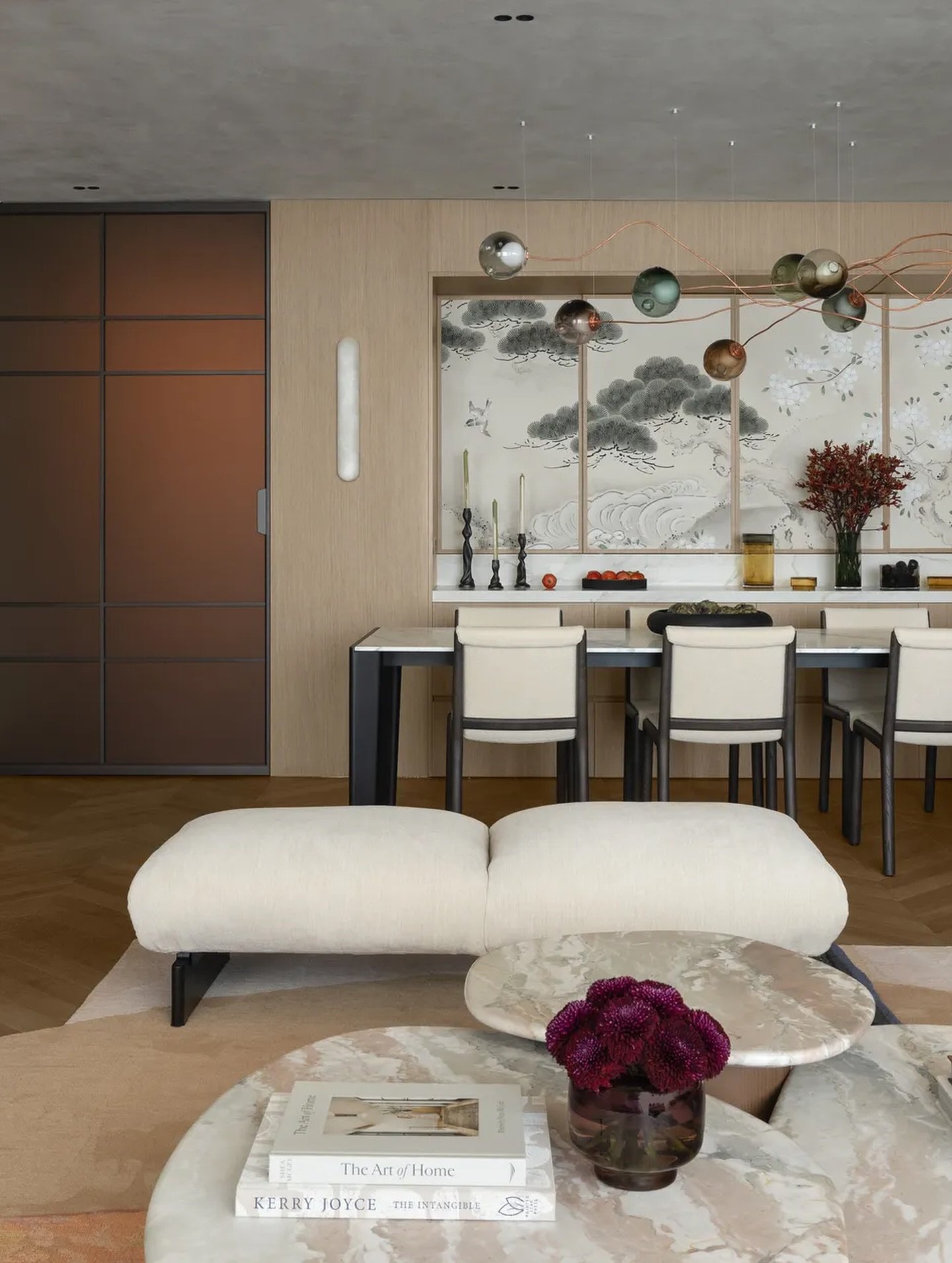 The living-dining sequence unfolds beneath a constellation of spherical pendants, herringbone flooring drawing the eye across zones.