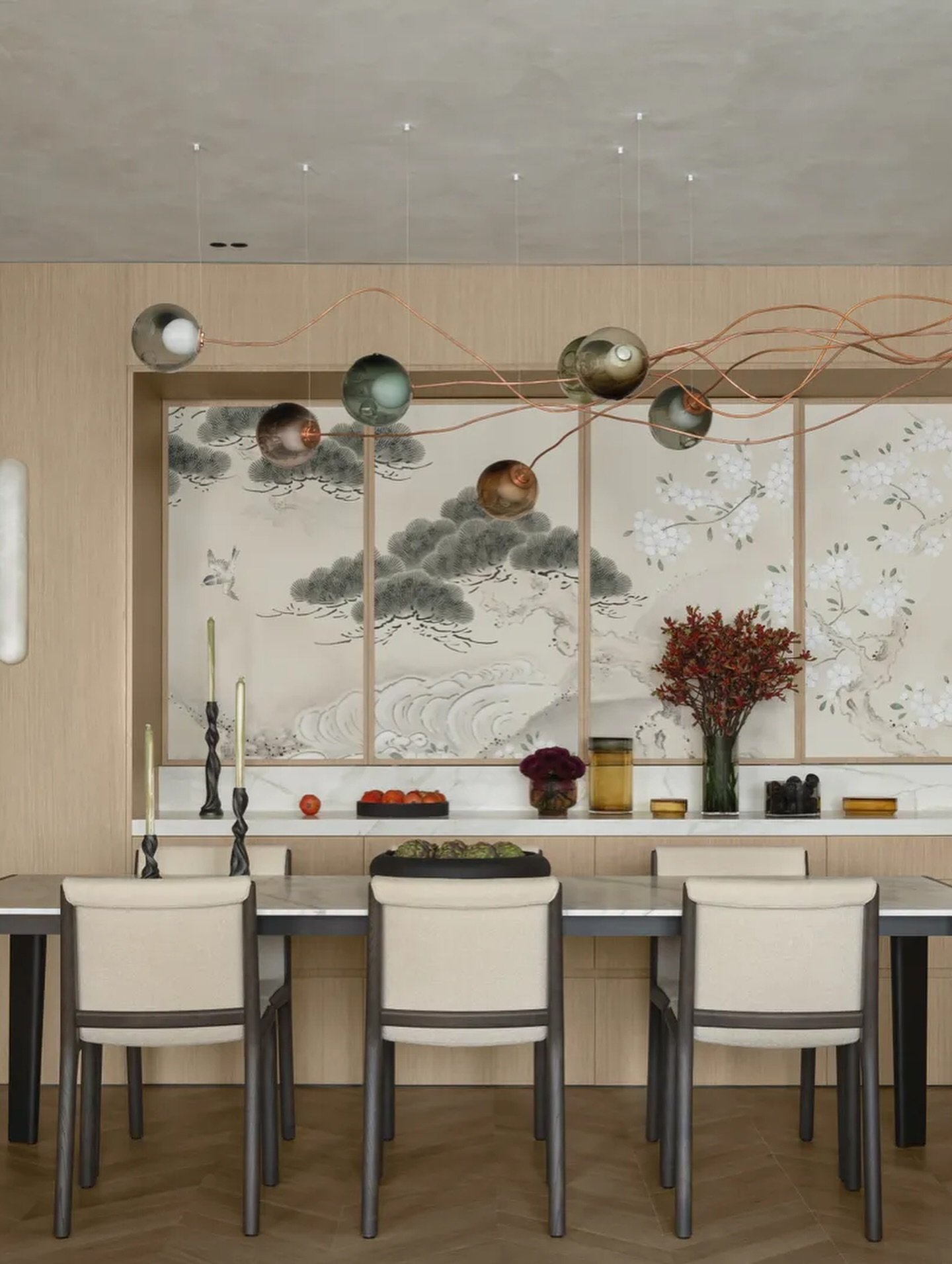 The dining wall's pine and blossom mural sets a soft, ink-wash counterpoint to the room's tonal restraint.