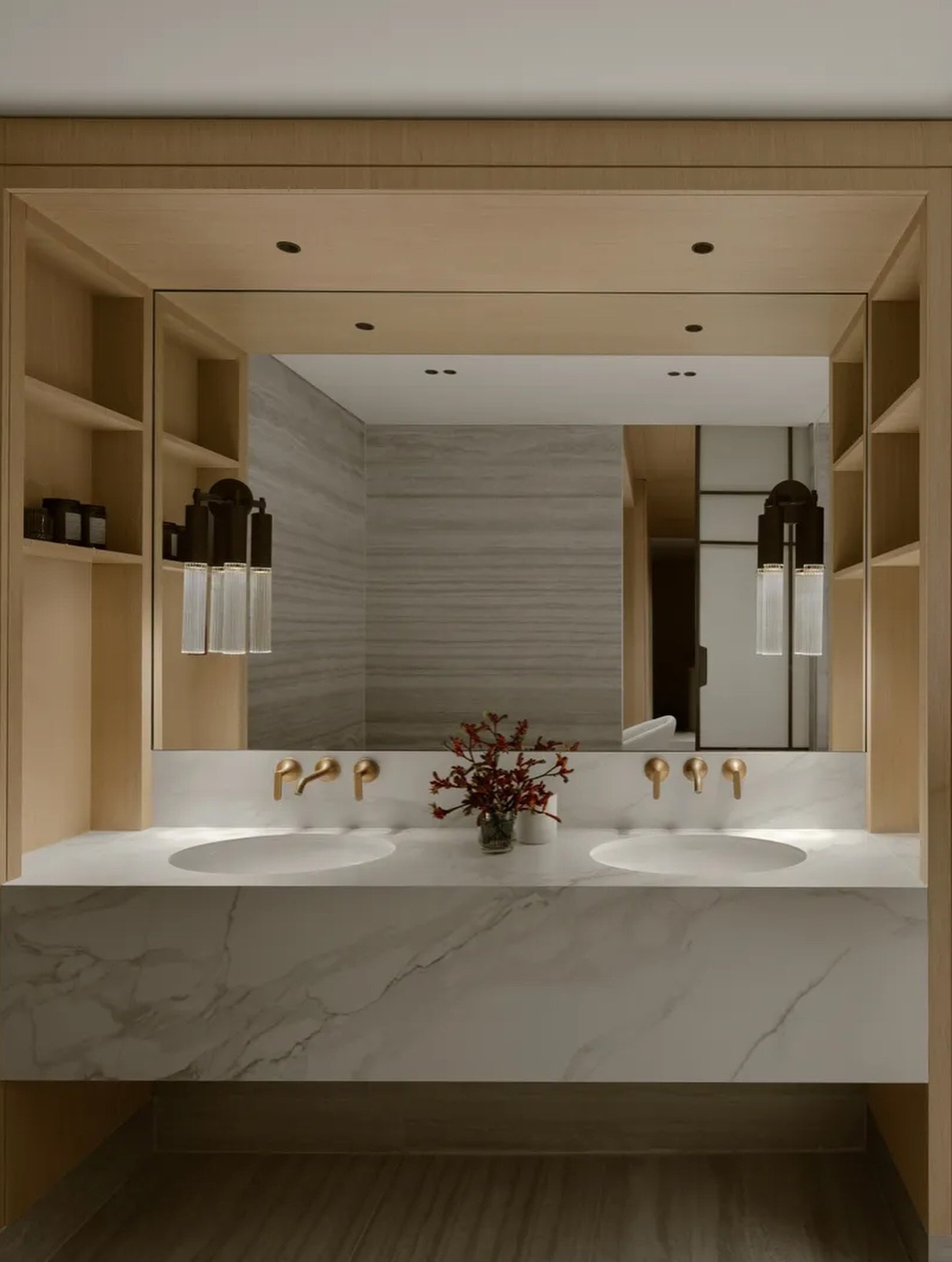 The bathroom's waterfall-edge marble vanity is warmed by a deep wood surround and slim brass sconces.