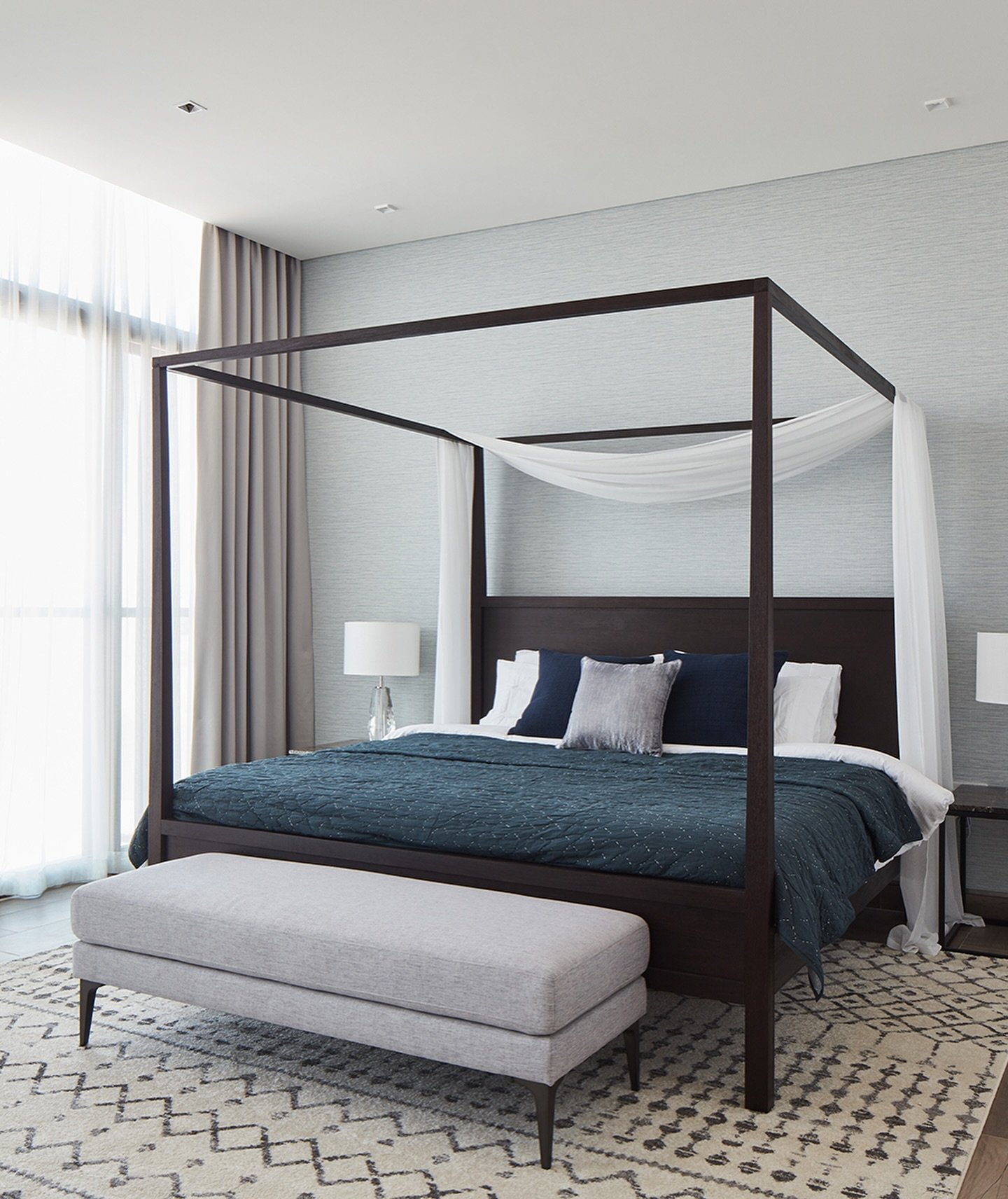 The bedroom composed as a cocoon, its dark wood frame softened by sheer drapery and layered textiles.