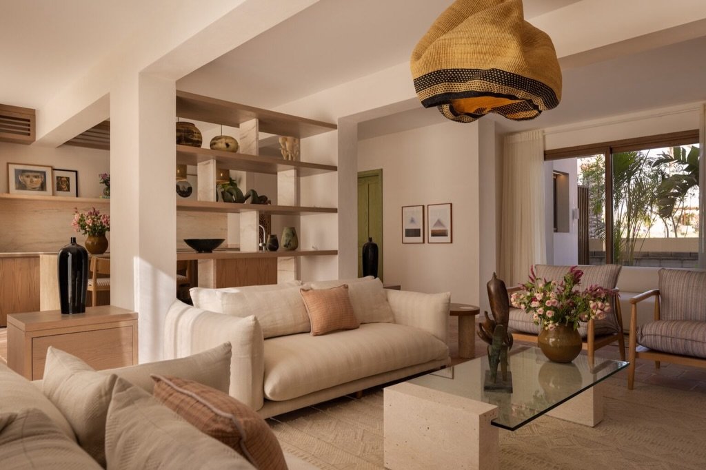 Layered textiles, ceramics on open shelving, and a rattan pendant give the seating area a tactile, inhabited stillness.
