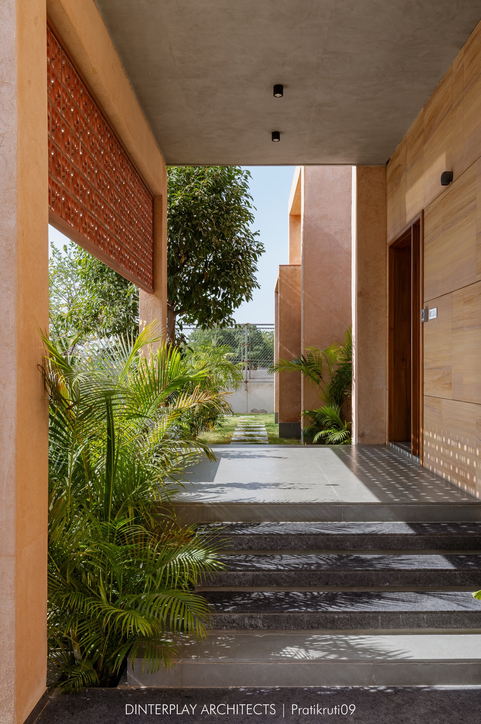 The entry verandah, where a terracotta jaali screen filters daylight across a sandstone-clad threshold