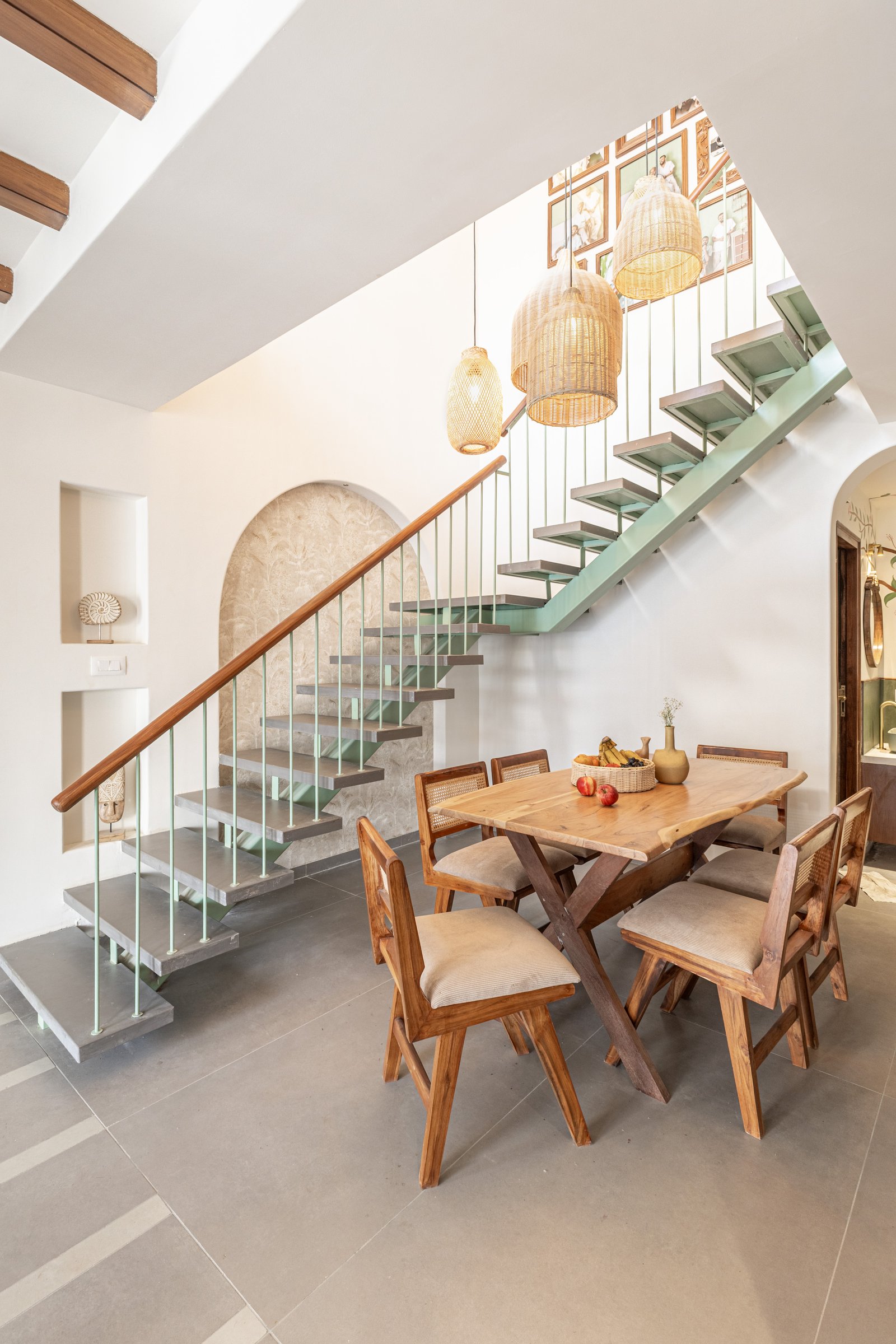 The dining area beneath the stair, where three woven cane pendants descend as a sculptural cluster