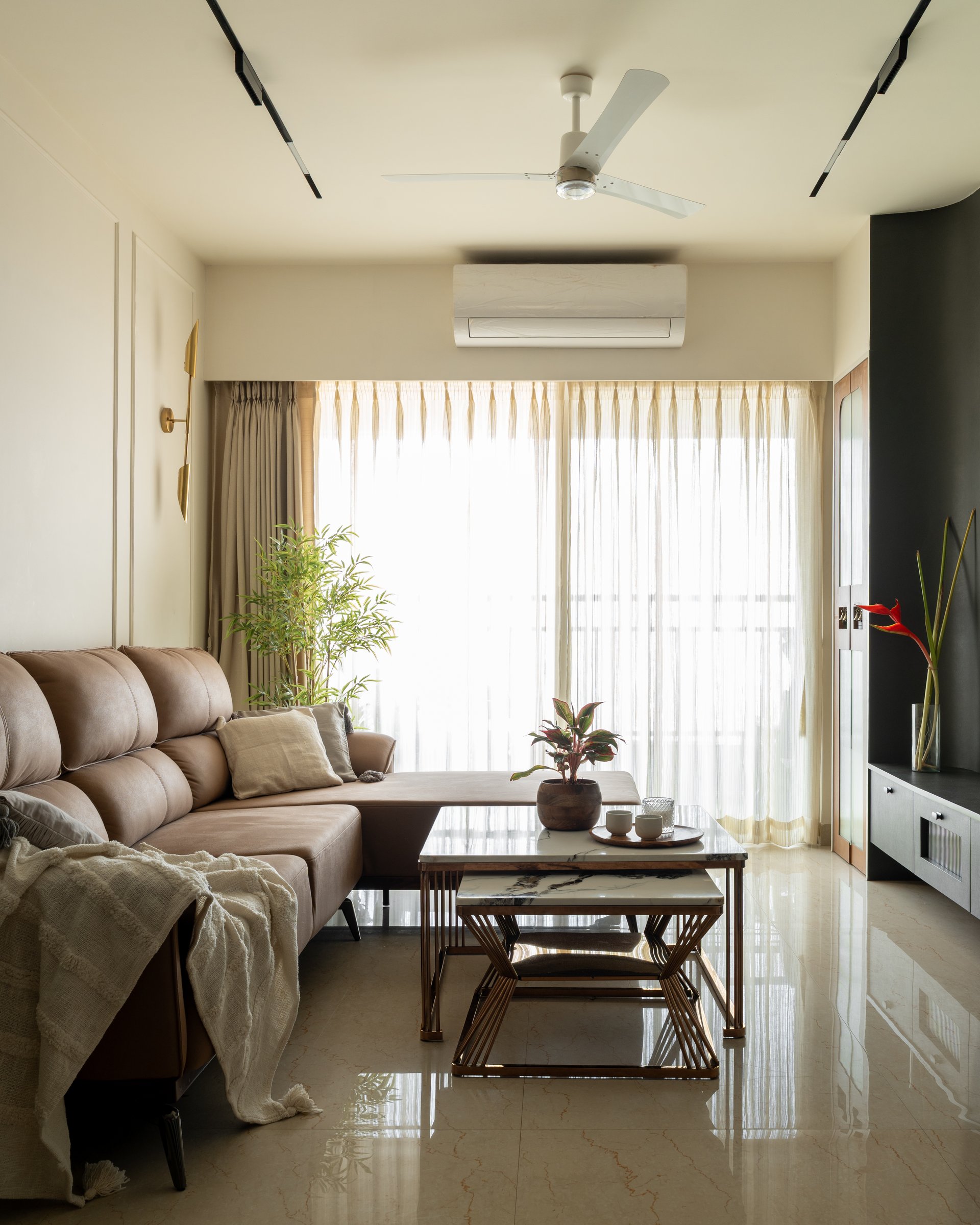 The living room, held between a panelled wall and a darker accent volume, with the balcony light filtered through sheer drapery