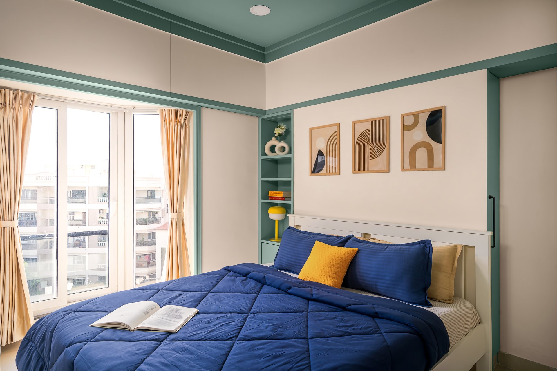 The first bedroom, organised around muted teal and warm cream with a graphic triptych above the bed