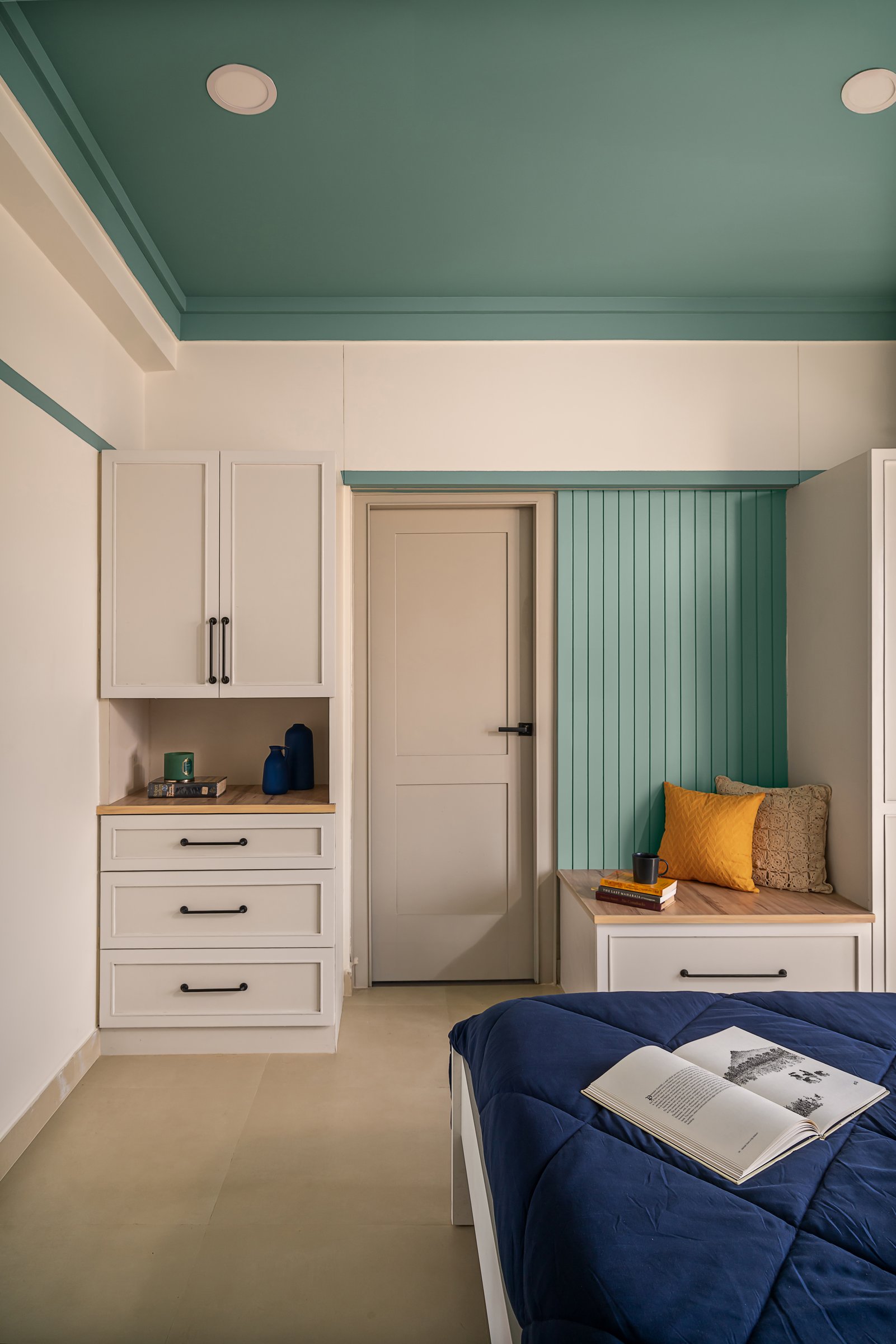 The ivory joinery wall with its shuttered wardrobe and a slim window seat in a teal-panelled alcove