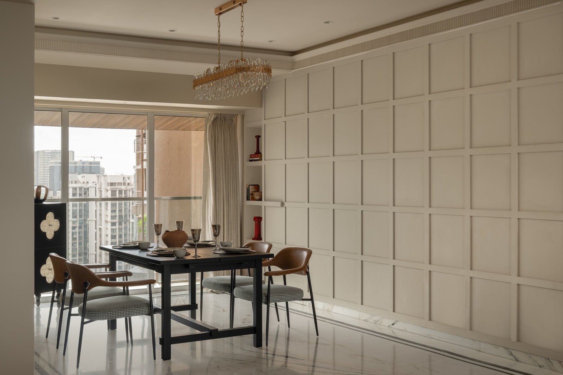 A gridded panelled wall runs floor to ceiling opposite the dining table, quiet architectural backdrop rather than decoration
