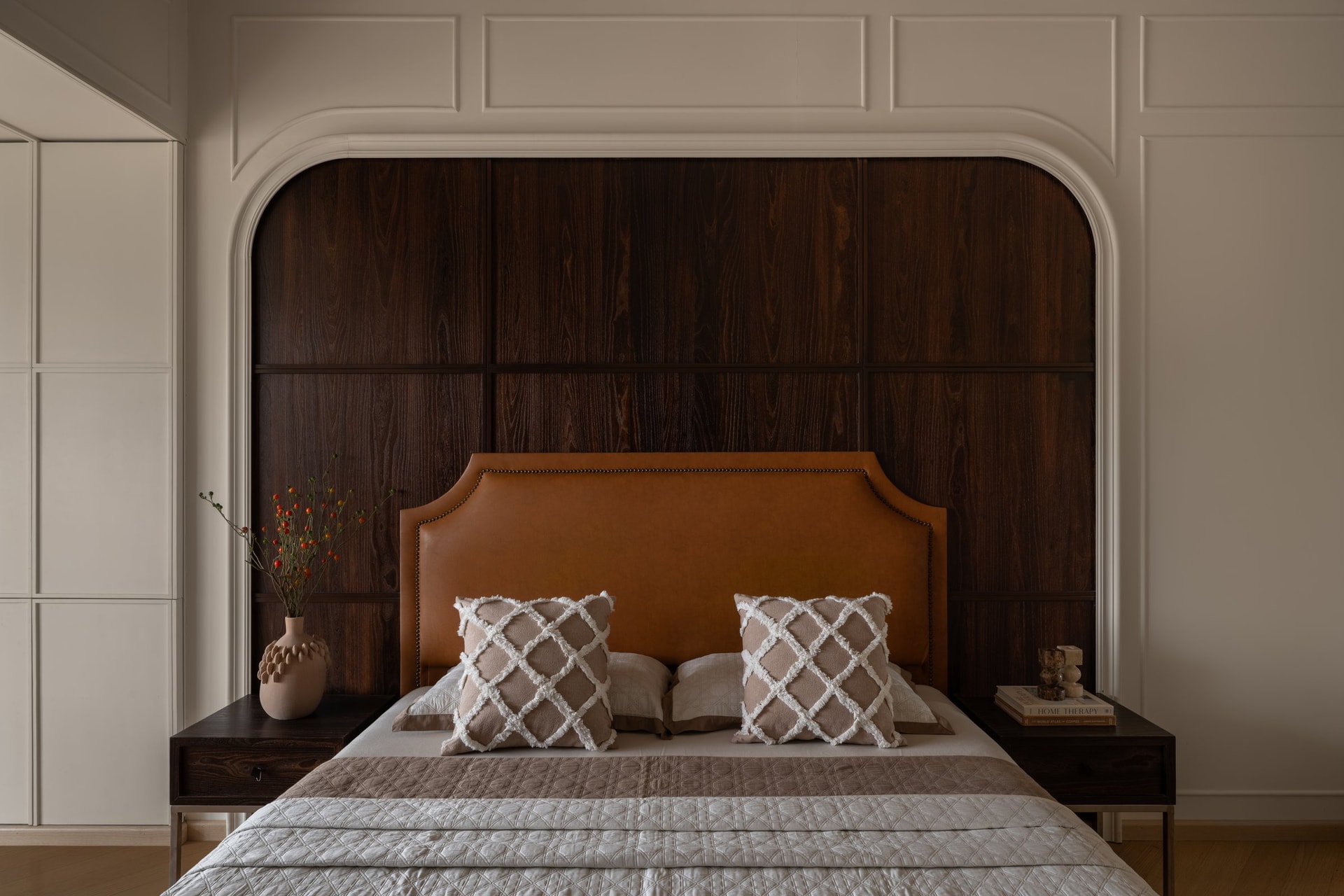 The master bedroom's arched niche in dark stained wood frames a tan leather headboard with brass stud detailing