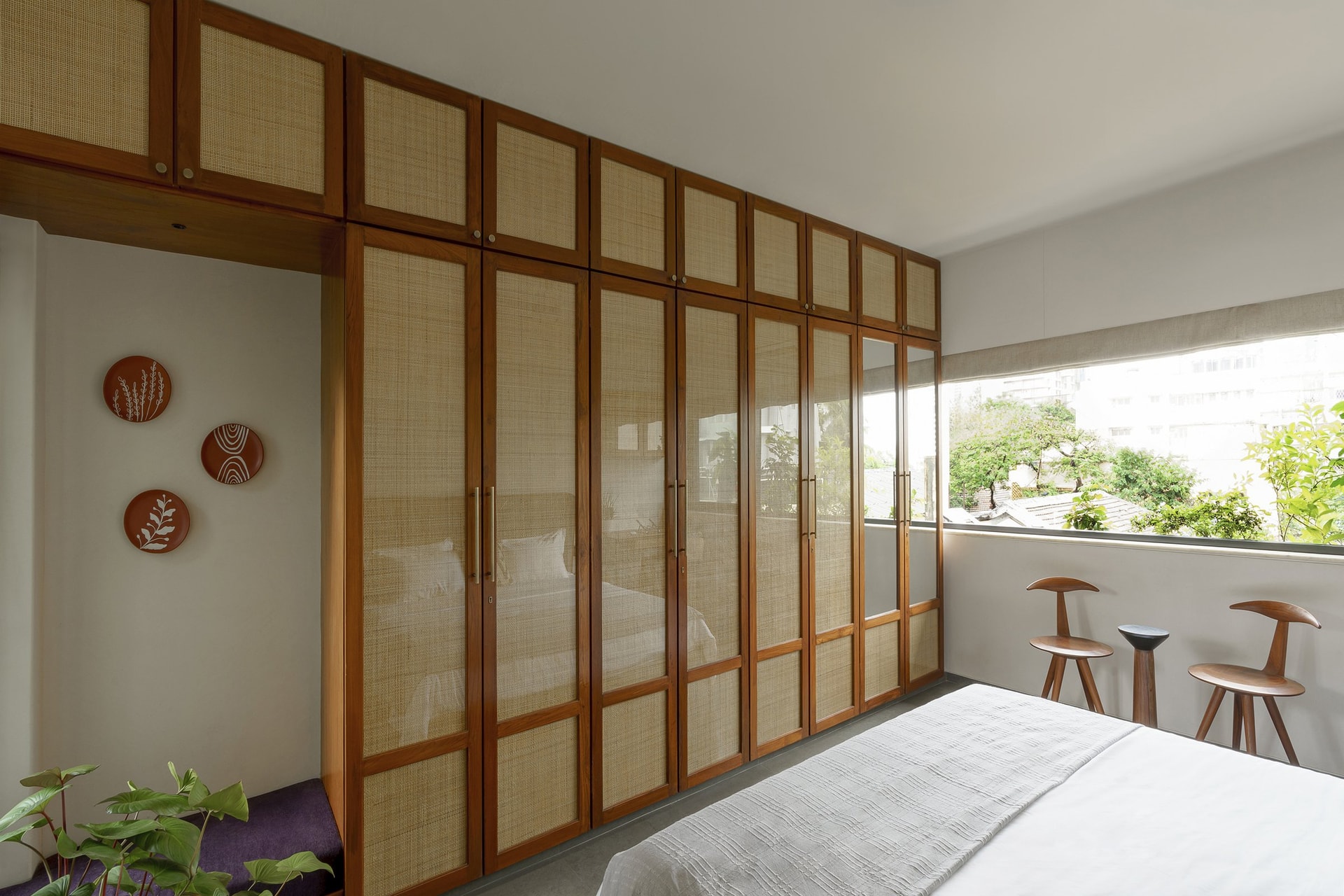 Cane-fronted wardrobes and hand-painted terracotta plates keep the room within the home's material family