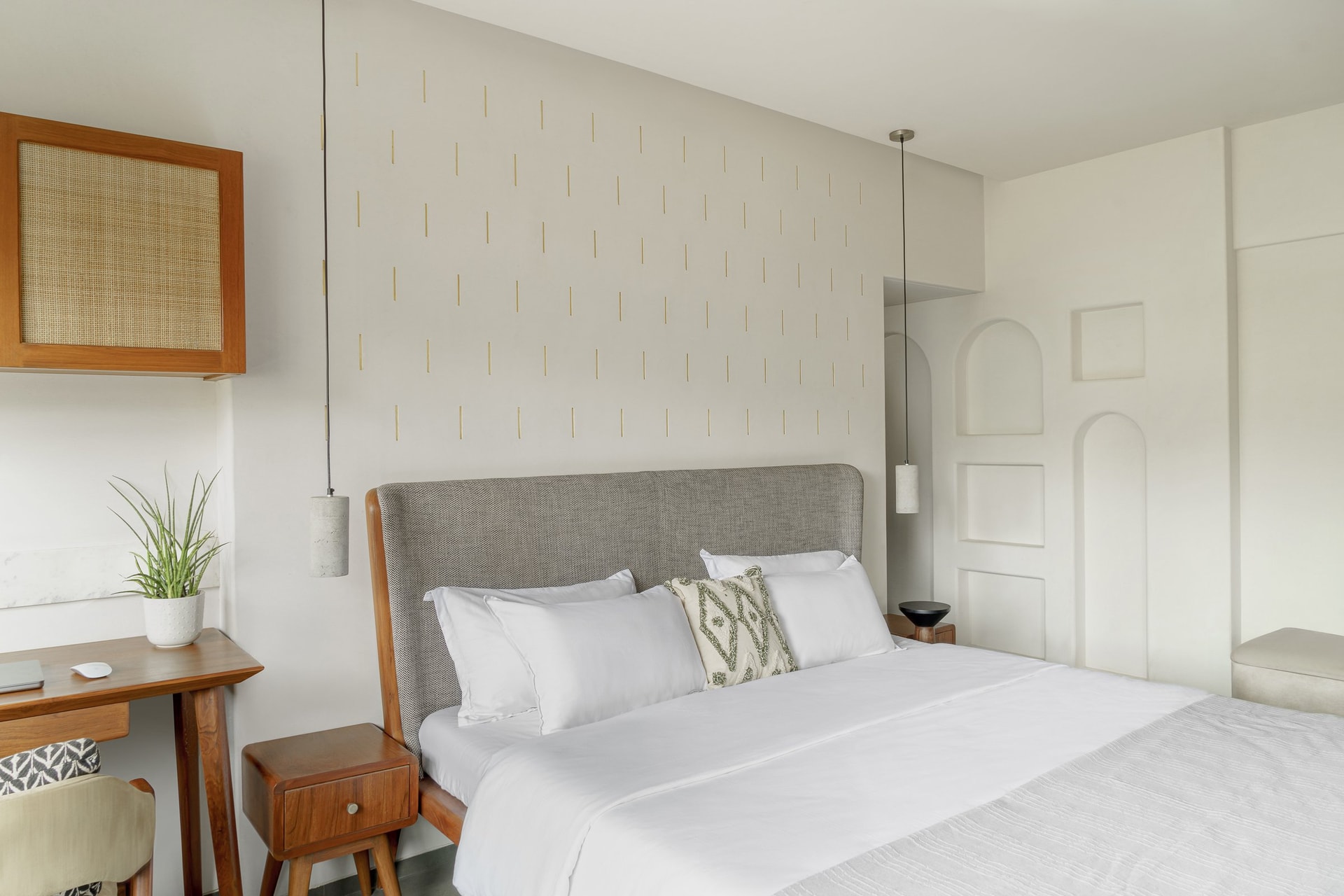 Above the bed, a hand-inlaid pattern of vertical brass strokes catches the light against the plaster