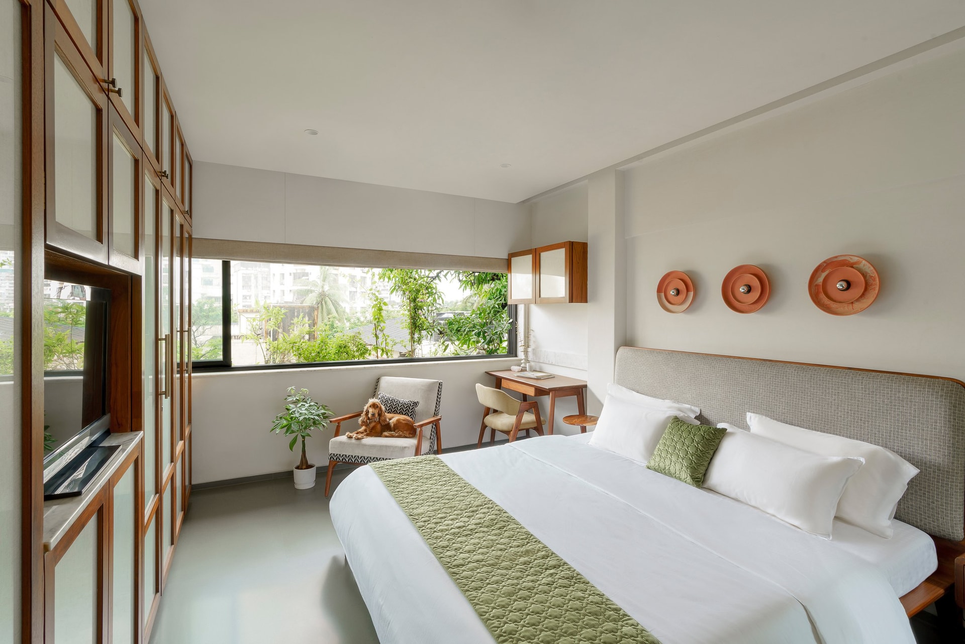The primary bedroom, grounded by three terracotta wall reliefs and framed by the tree canopy outside