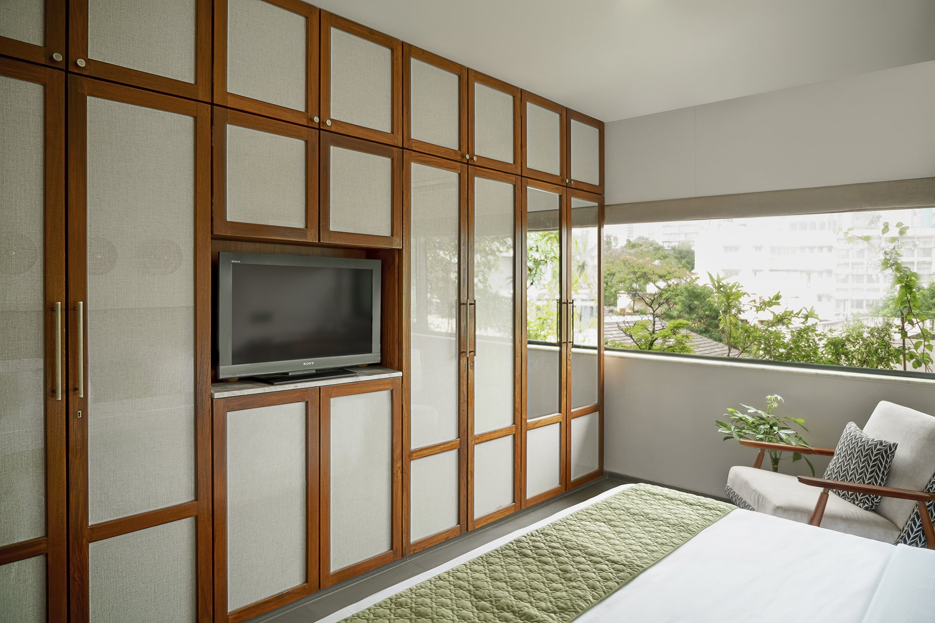 The second bedroom, where a full wall of wood-and-fabric joinery integrates wardrobe and media into one plane