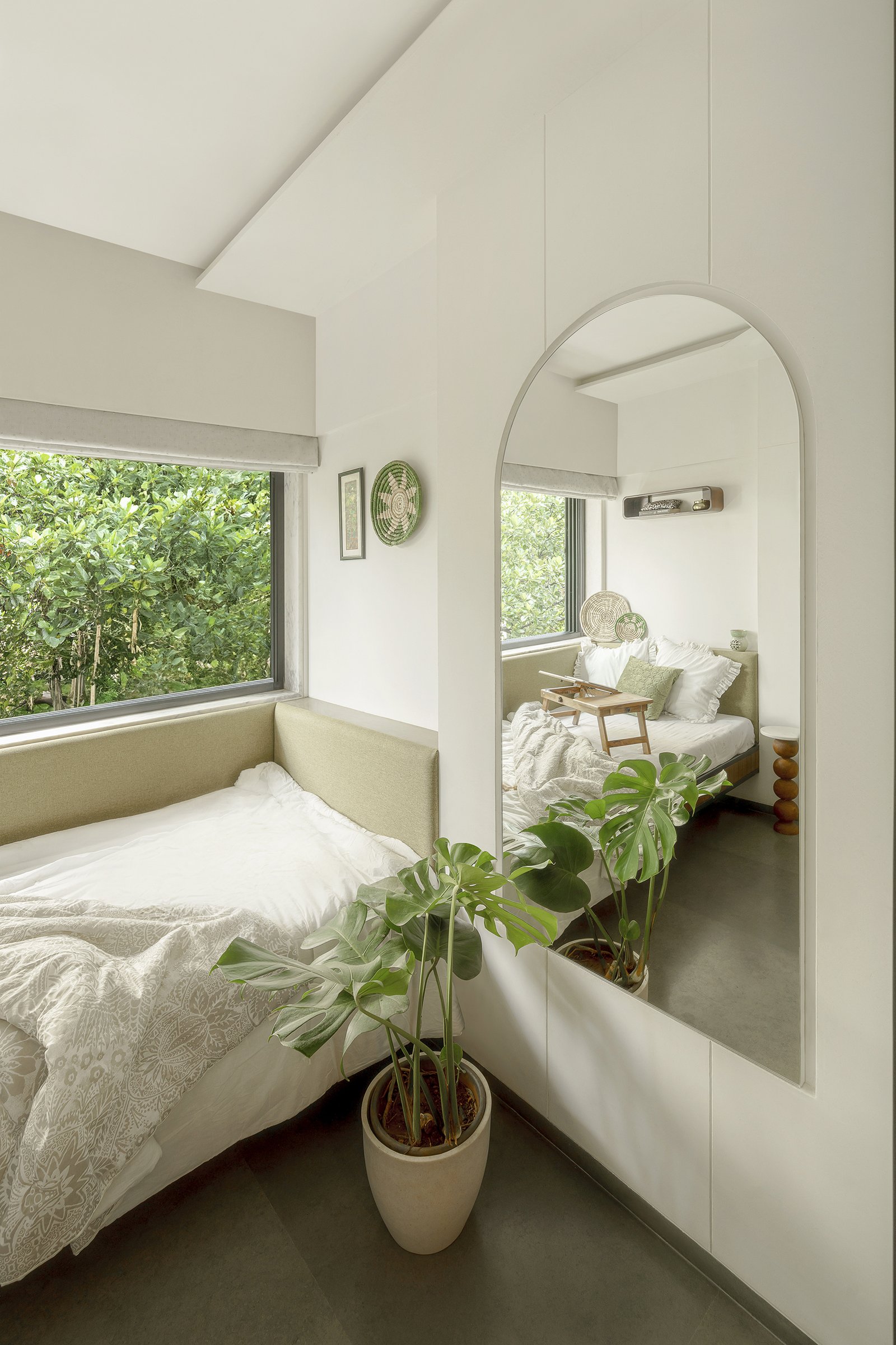 The third bedroom, where a daybed sits beneath the window and an arched mirror reflects the foliage back in