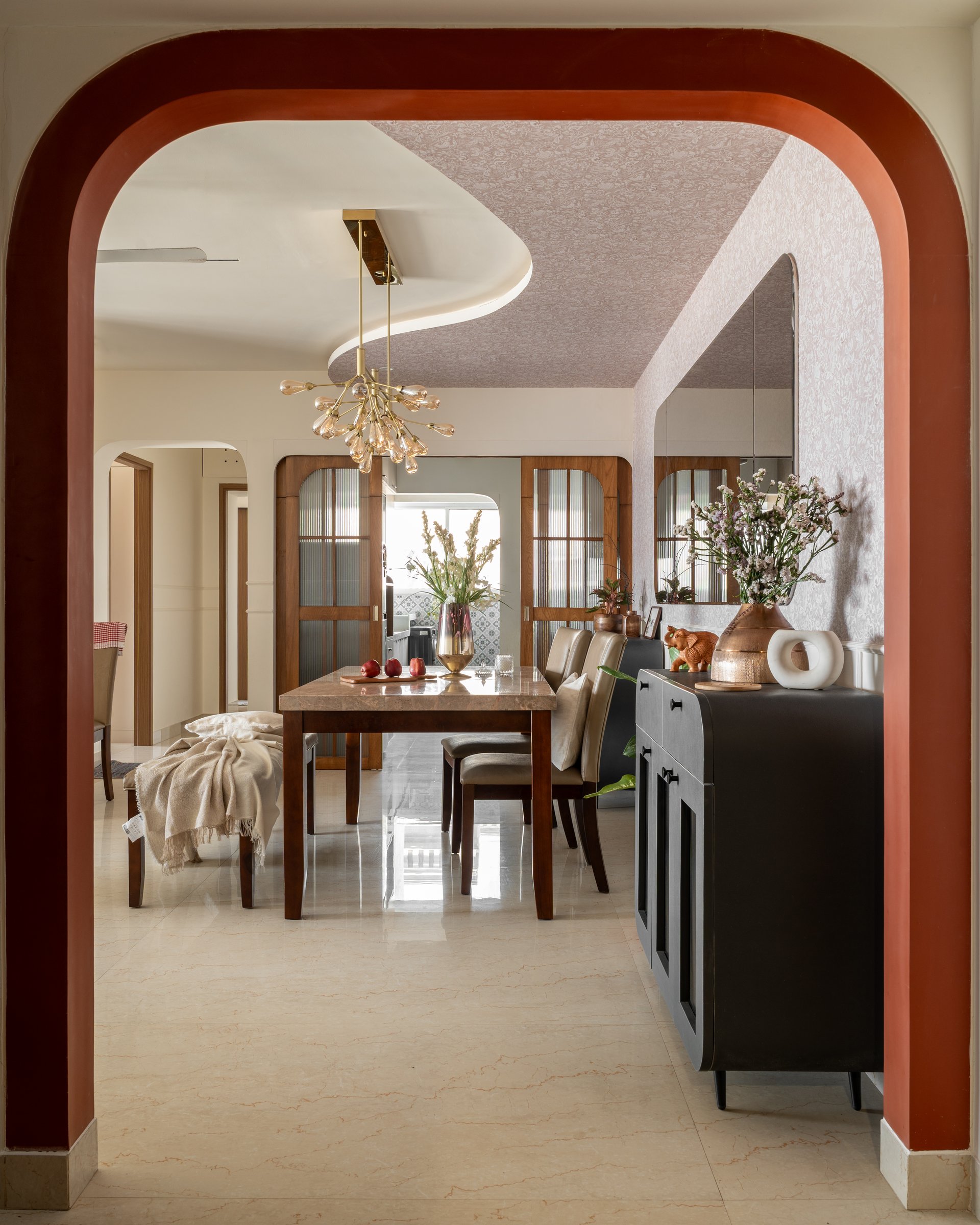 Through the arch, the inherited dining table and chairs sit beneath a brass chandelier of clustered amber bulbs