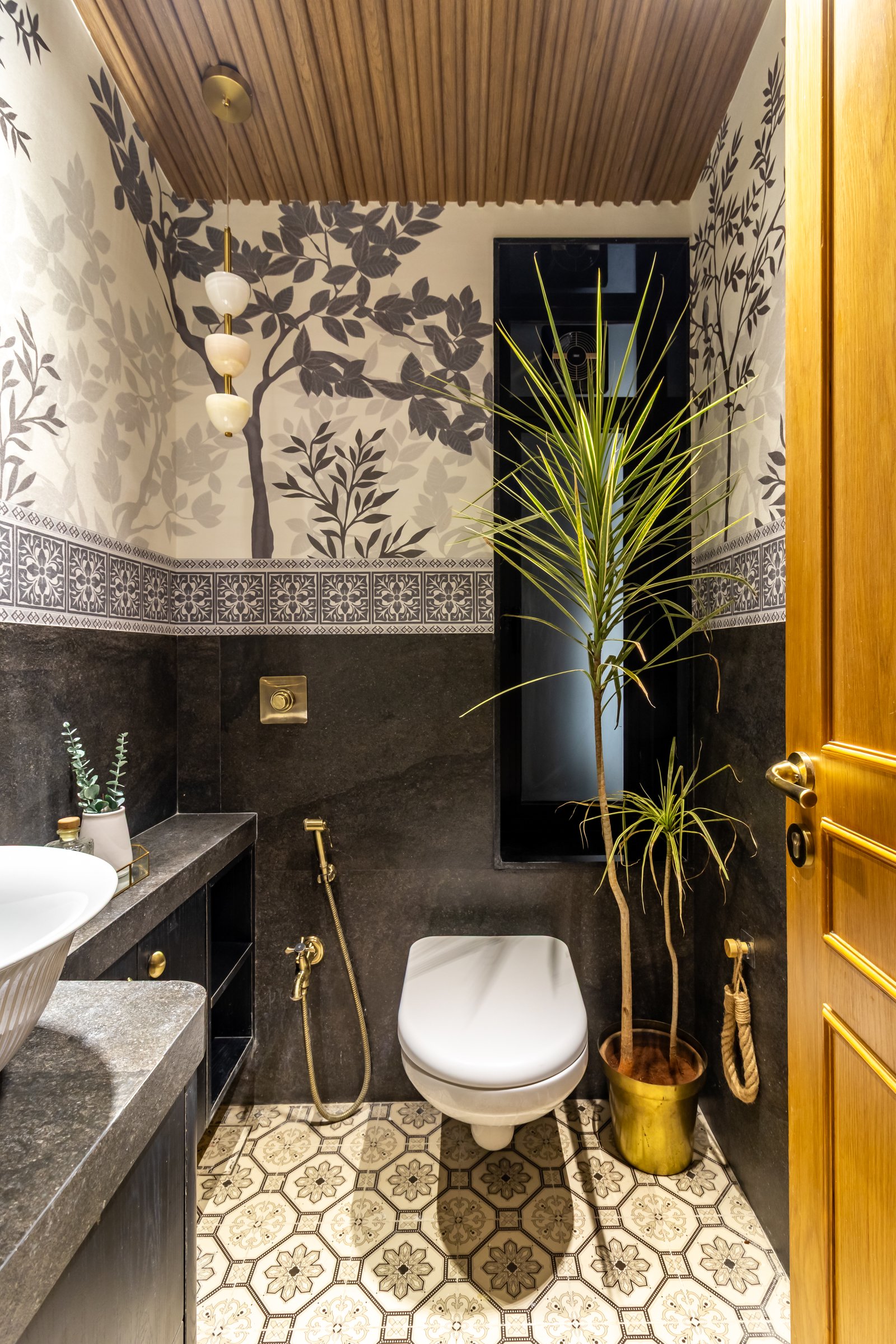 The powder room, wrapped in botanical wallpaper above a dark stone dado
