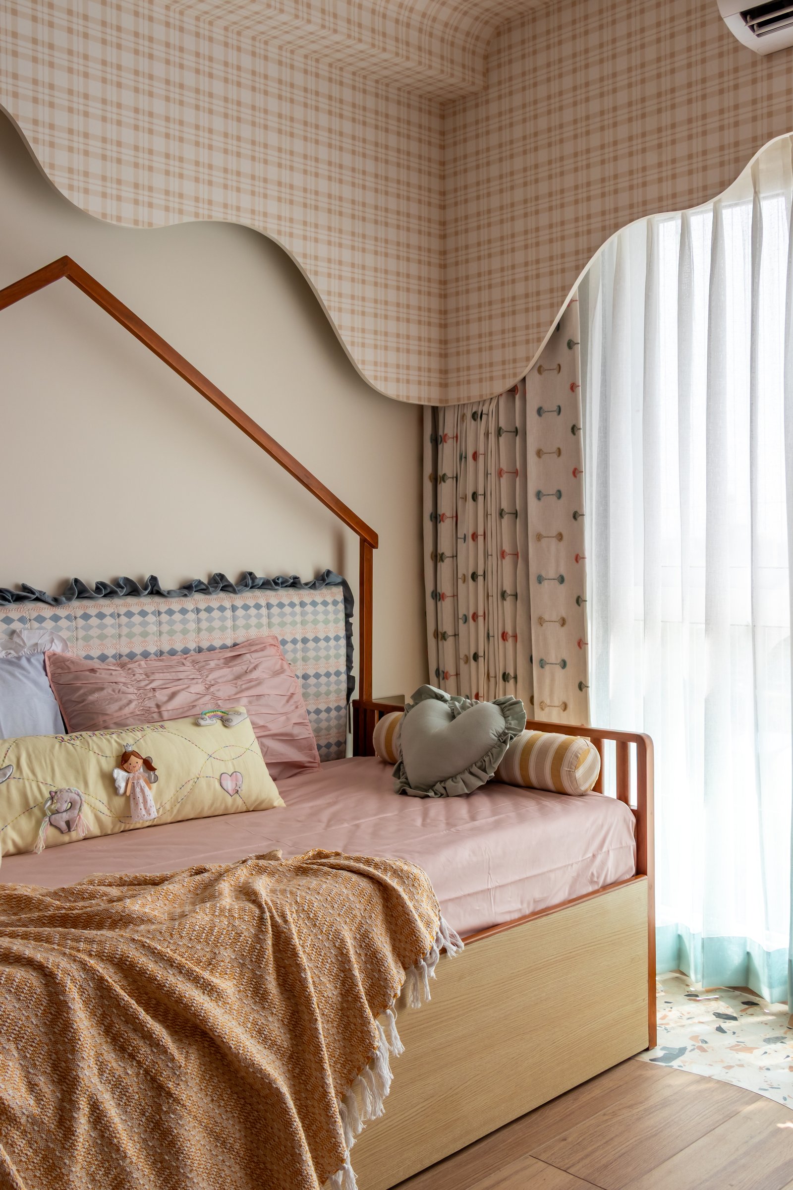 The children's bedroom, where a house-shaped timber bed frame stands beneath a wavy gingham-wrapped cornice