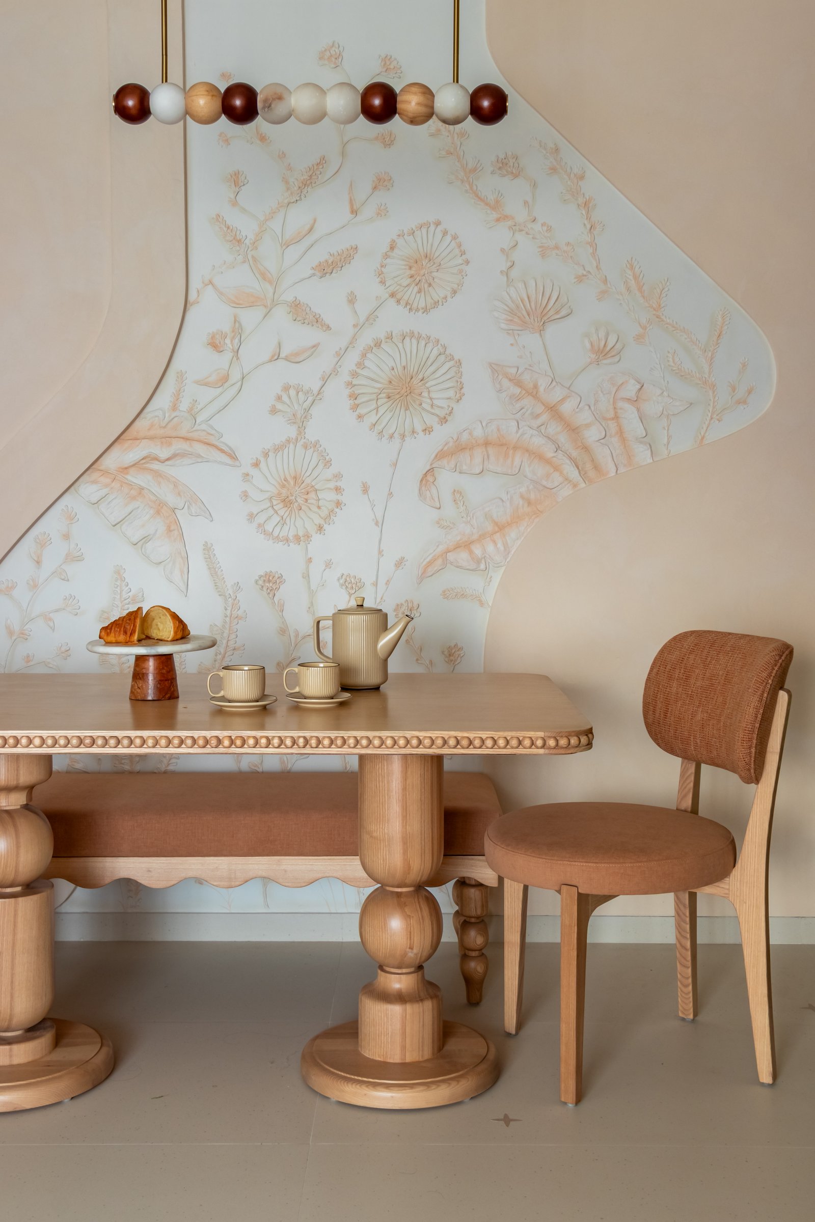 The dining area, defined by a hand-sculpted botanical mural in pale sage and rust bas-relief